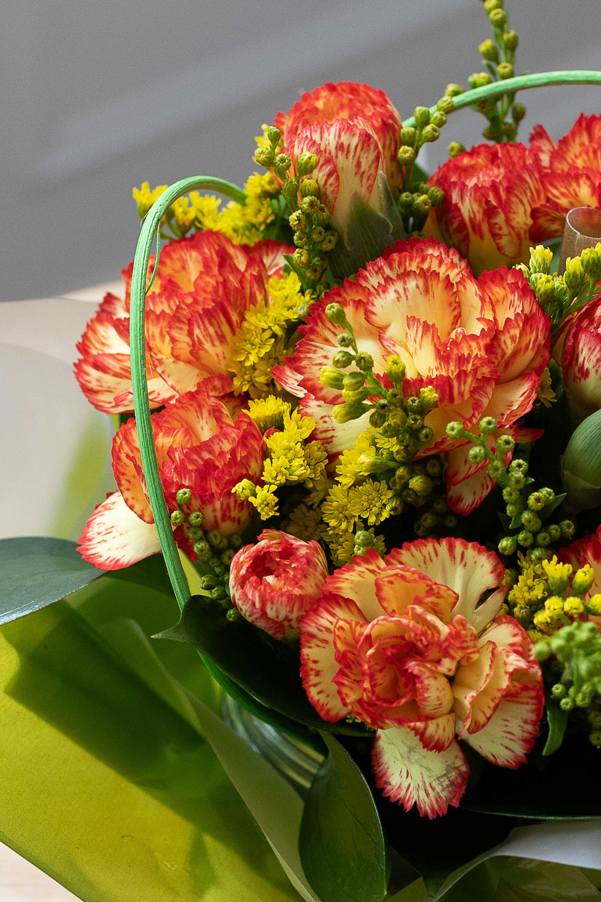 Close-up of orange-and-yellow variegated carnations with yellow filler flowers and green foliage in a posy.