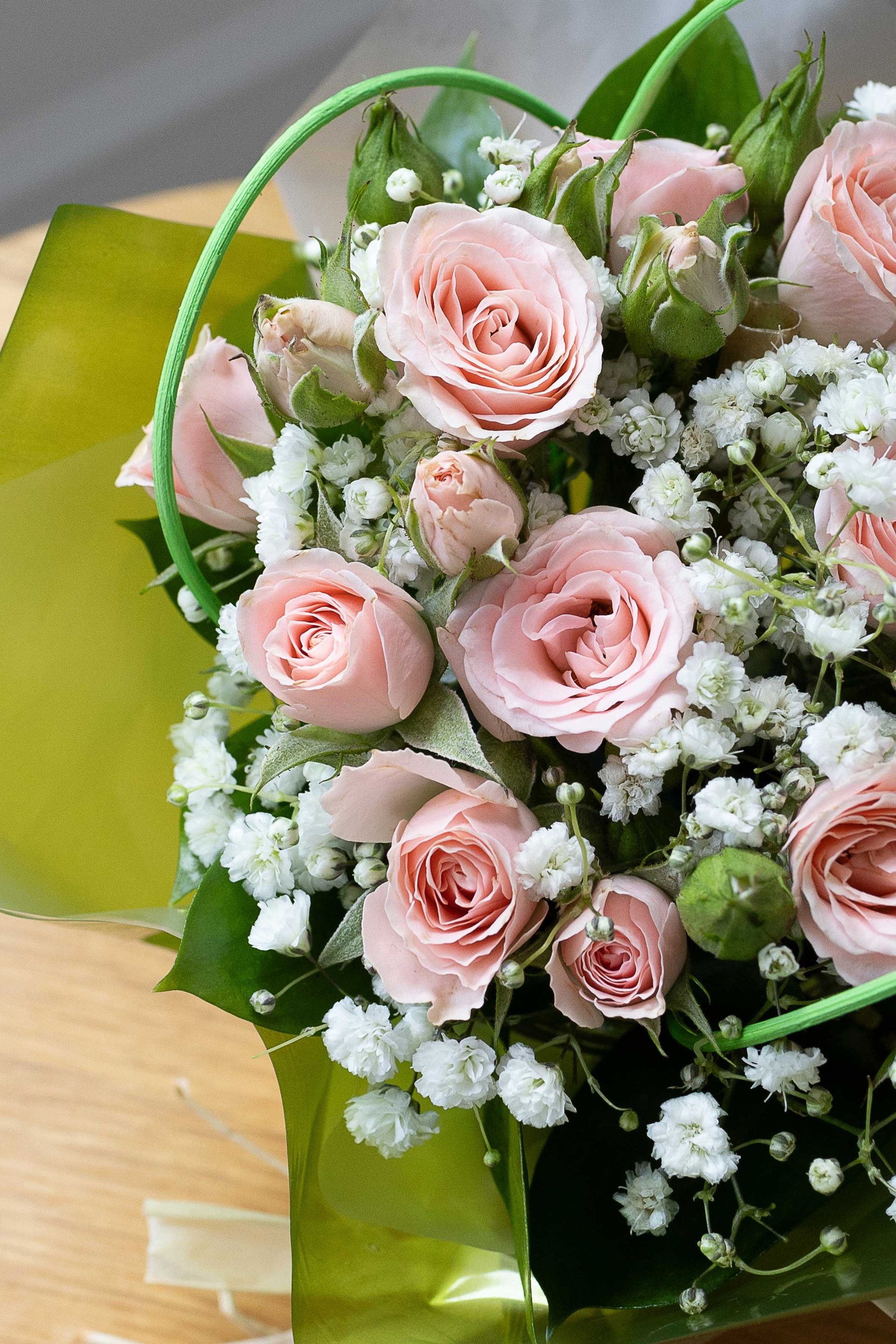 Close-up of pale pink roses and white baby's breath arranged in a posy with green foliage and wrapping.