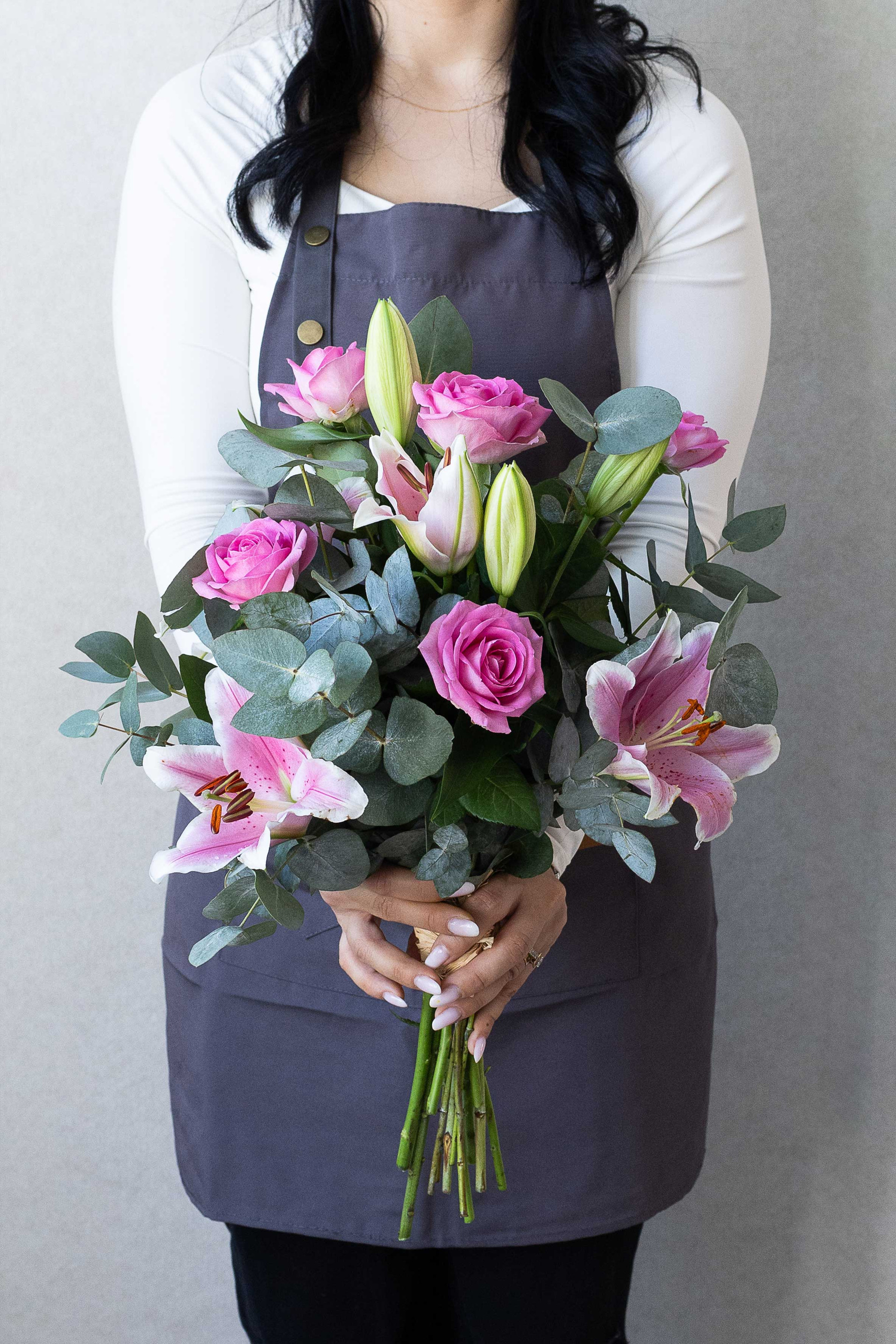 Florist holding a bouquet of pink roses, pink lilies, and eucalyptus against a gray background.