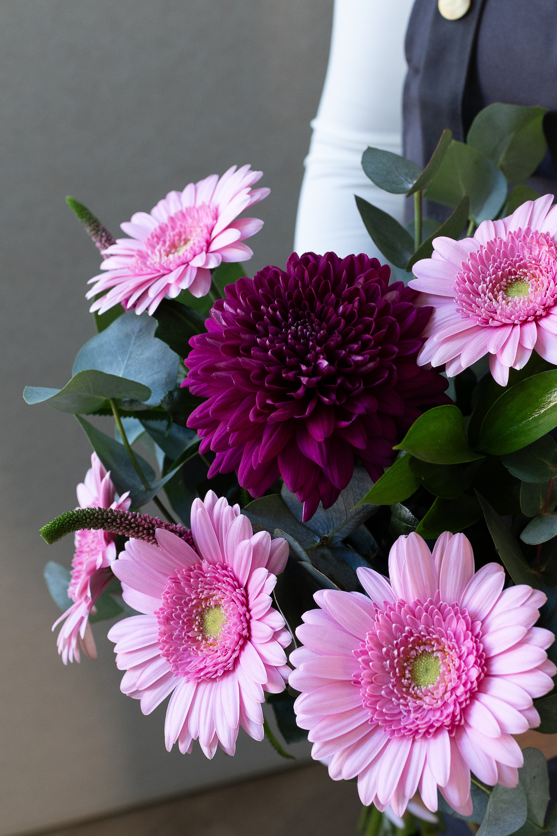 Close-up of pink gerbera daisies, a burgundy chrysanthemum, eucalyptus, and veronica flowers.