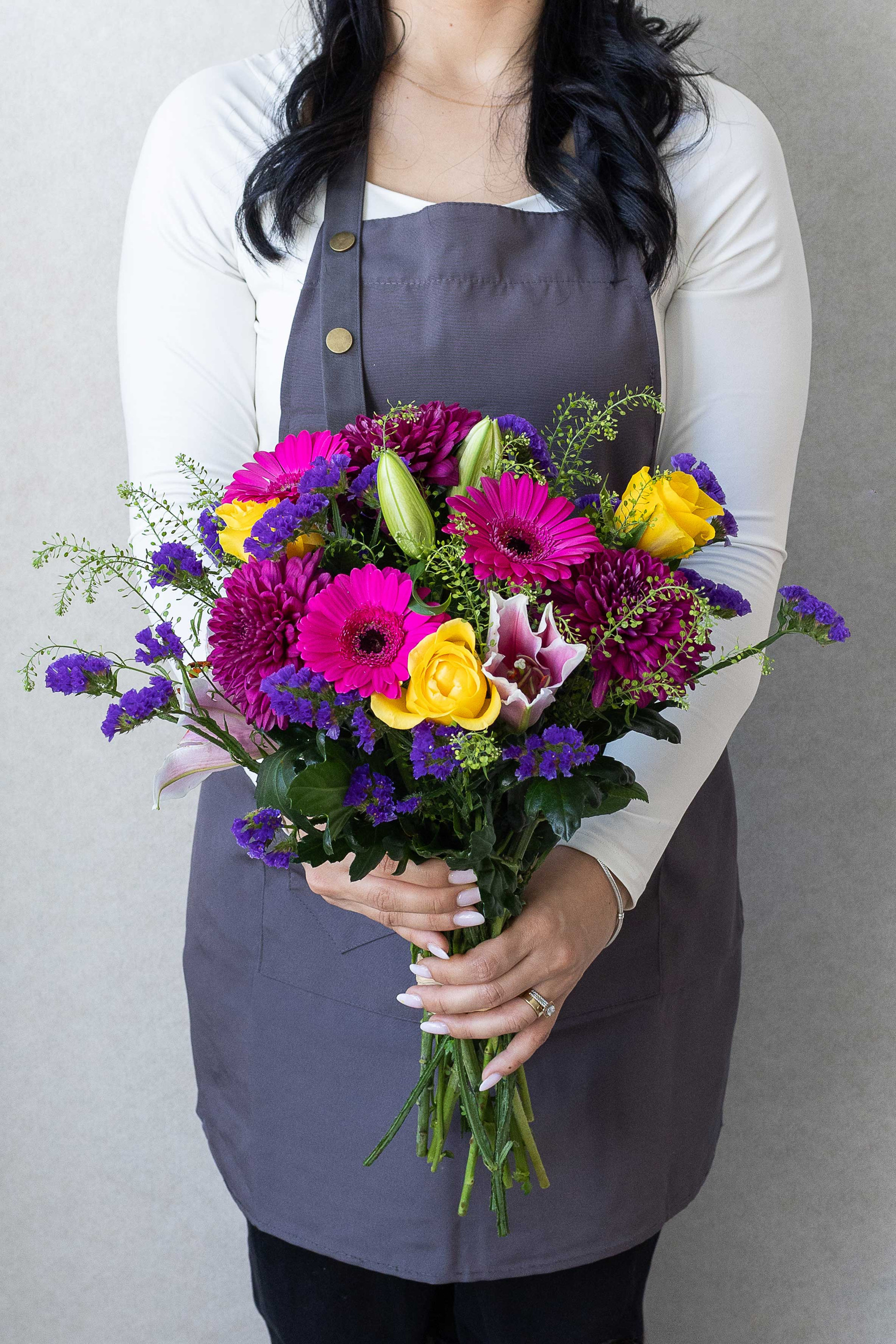 Florist holding a vibrant bouquet of gerberas, chrysanthemums, roses, lilies, and purple statice flowers.