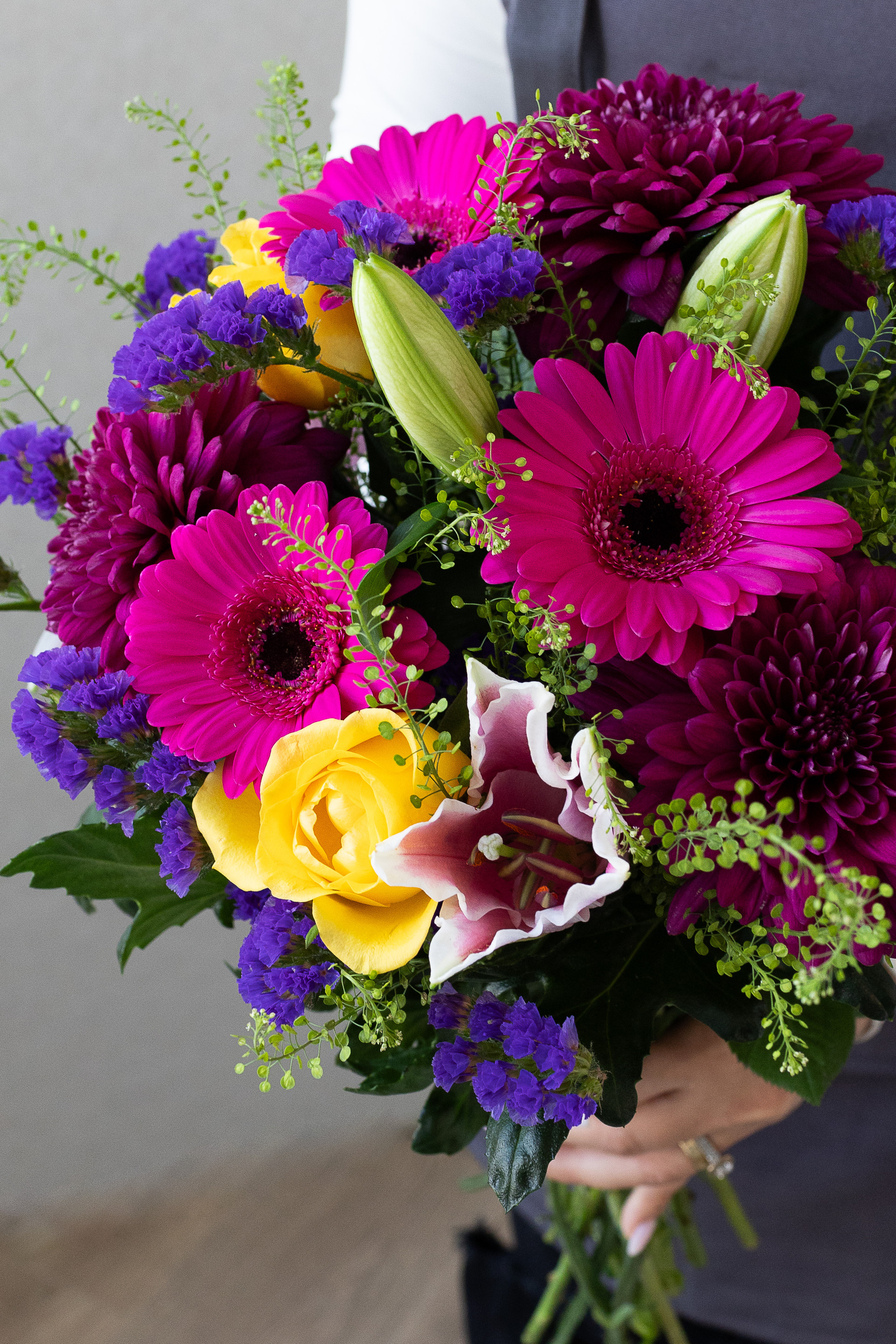 Close-up of magenta gerberas, burgundy chrysanthemums, yellow roses, pink lilies, and purple statice.