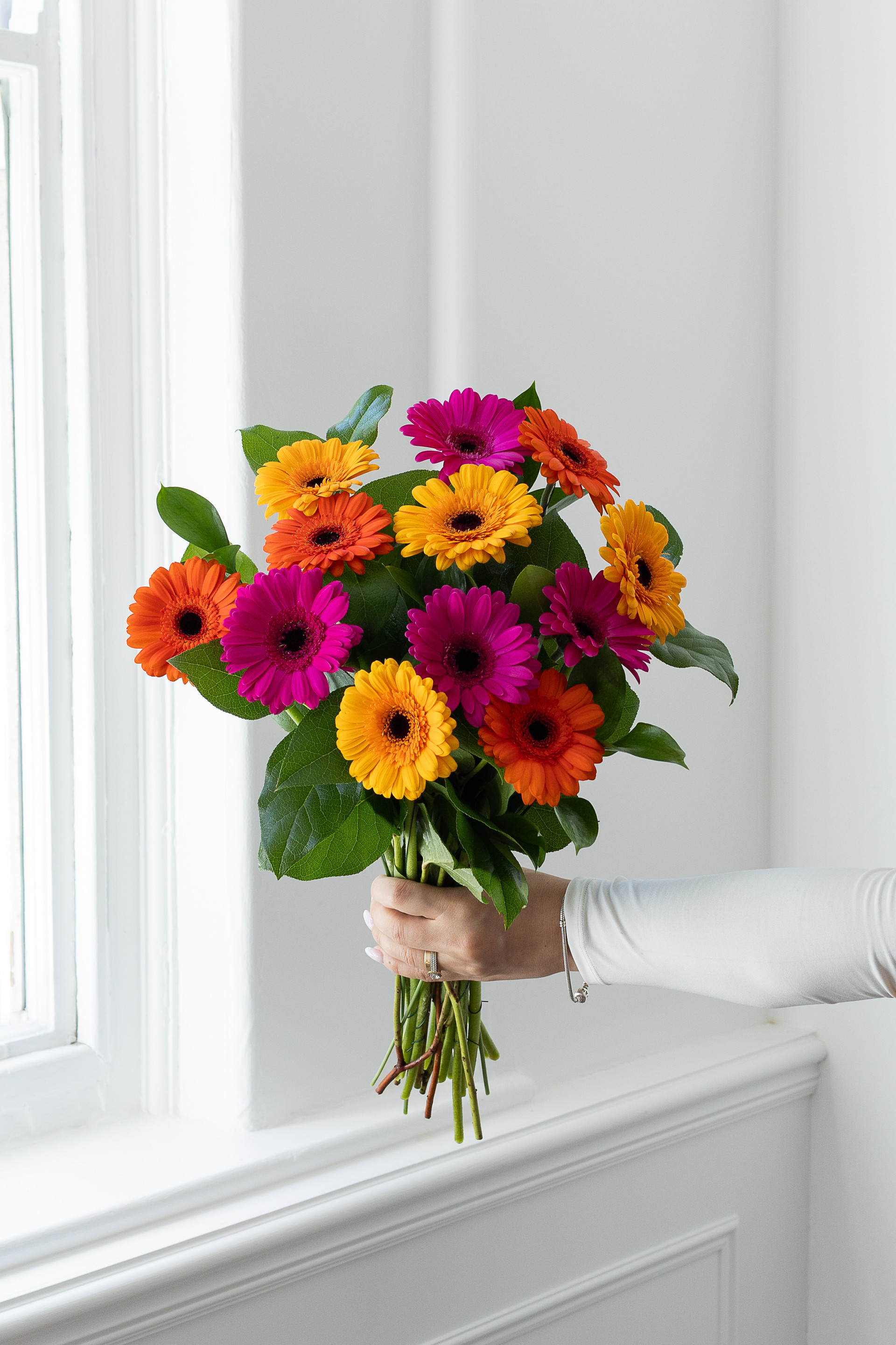 Mixed pink, orange, and yellow gerbera bouquet by a window.