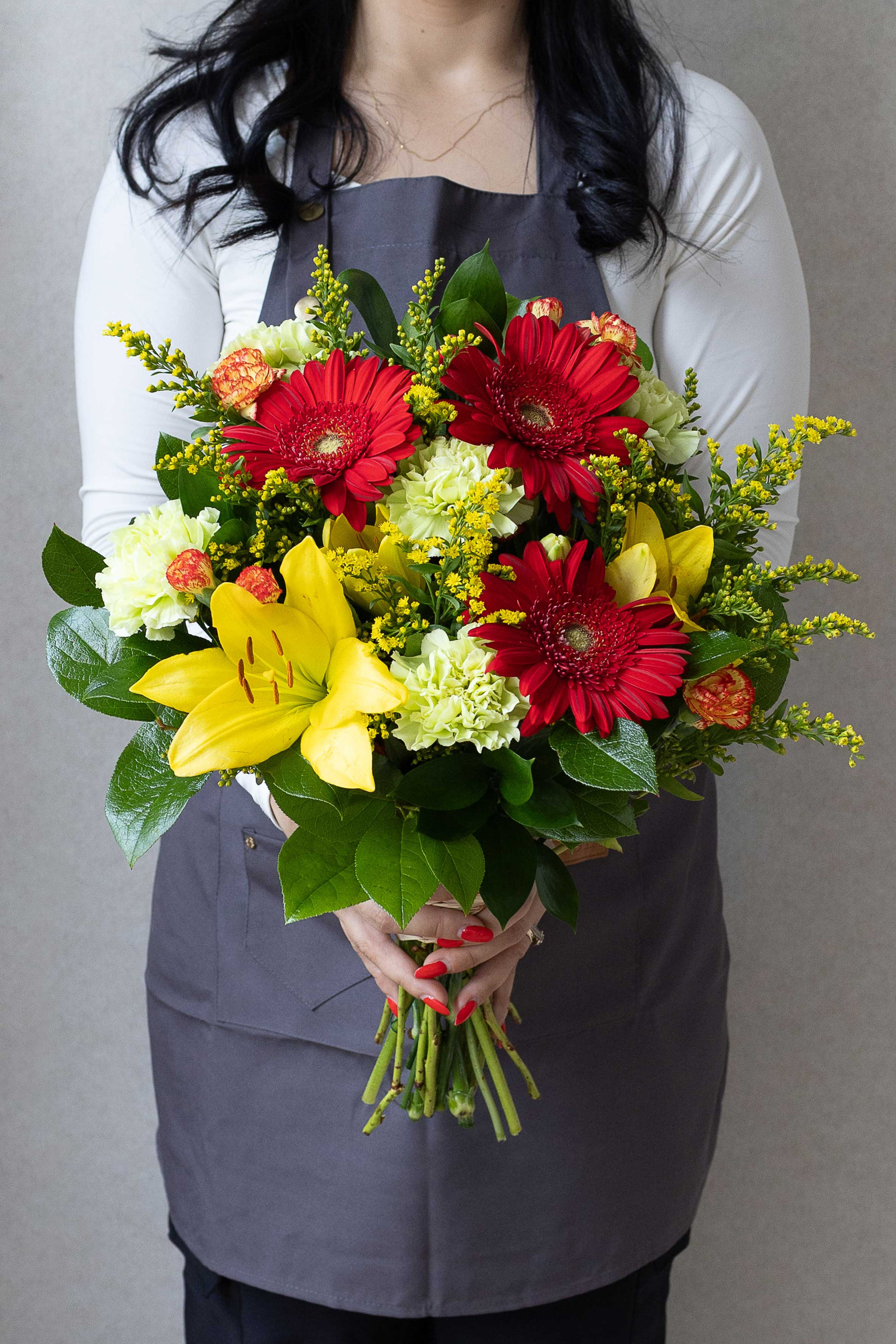 Hand-tied bouquet with red gerberas, yellow lily, and green carnations.