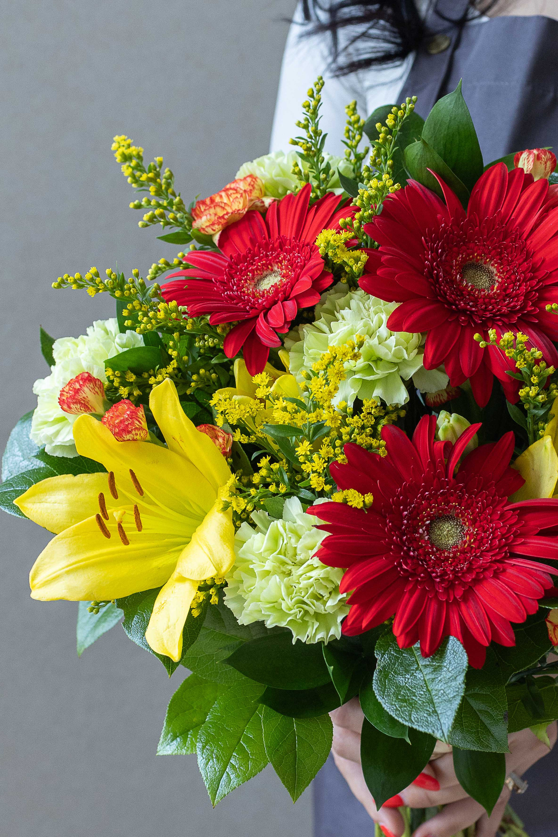 Close-up of red gerberas, yellow lily, carnations, and yellow filler flowers.