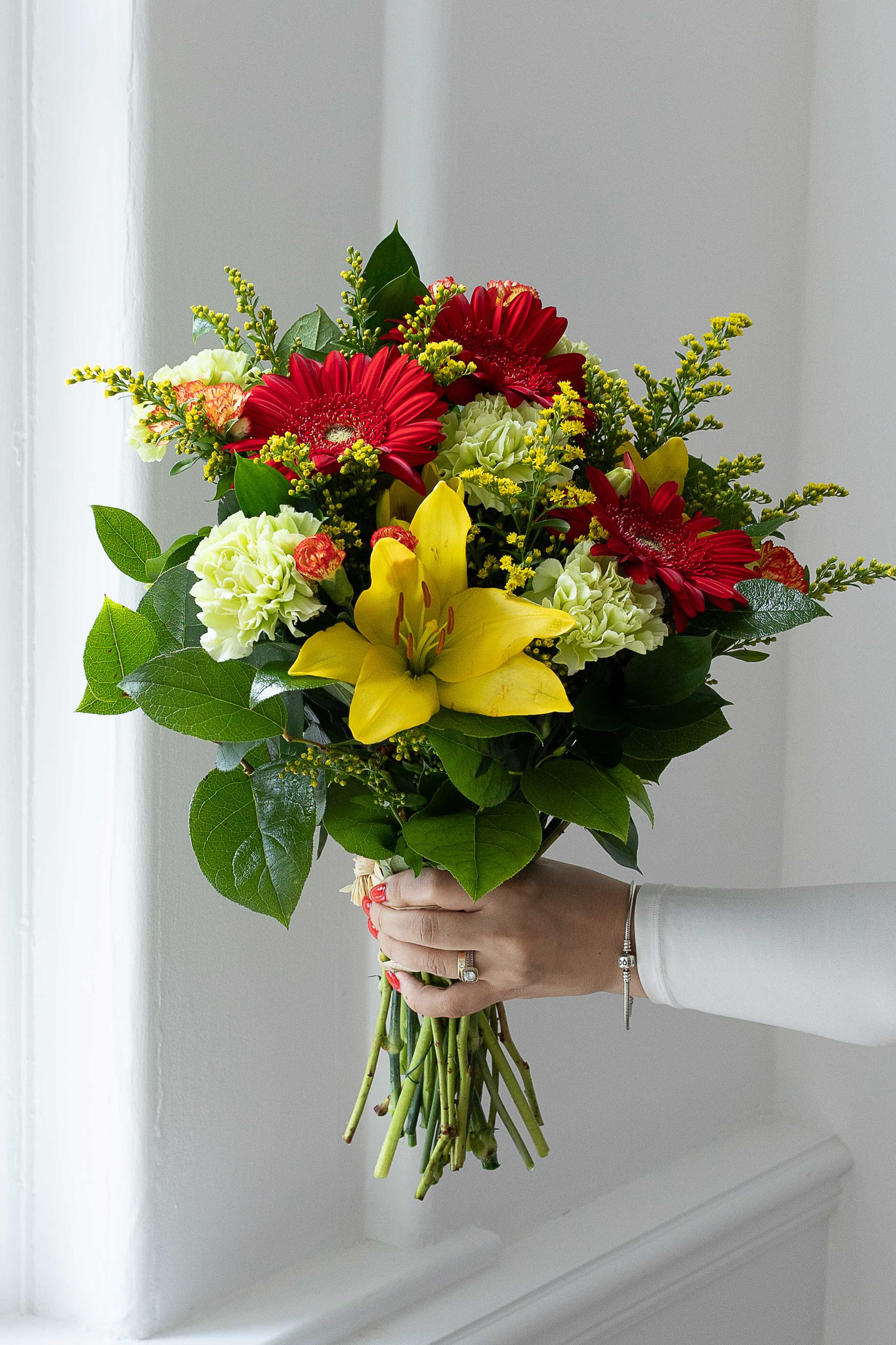 Bright bouquet with red gerberas, yellow lily, green carnations, and solidago.