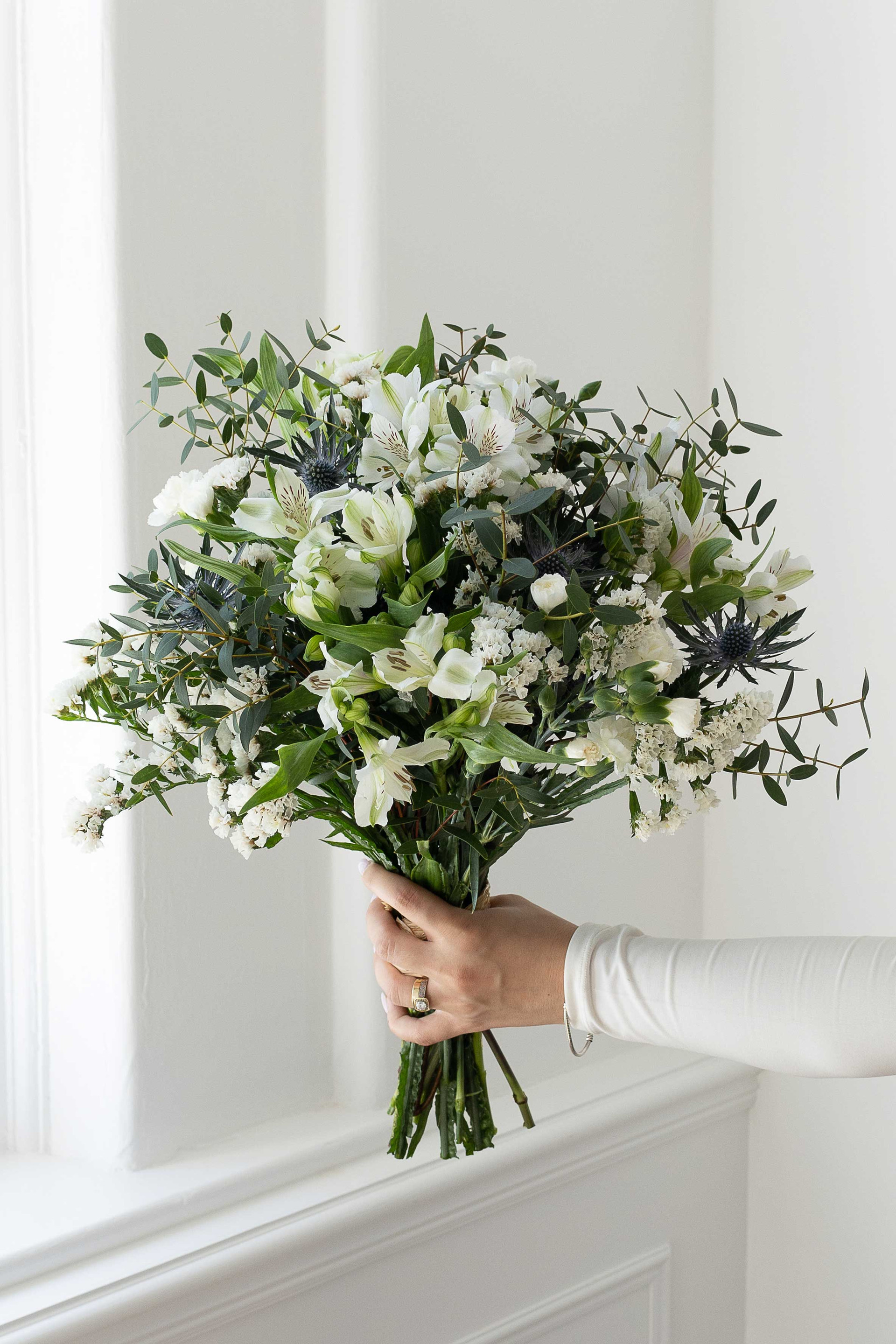 White floral bouquet with eucalyptus and blue thistles.