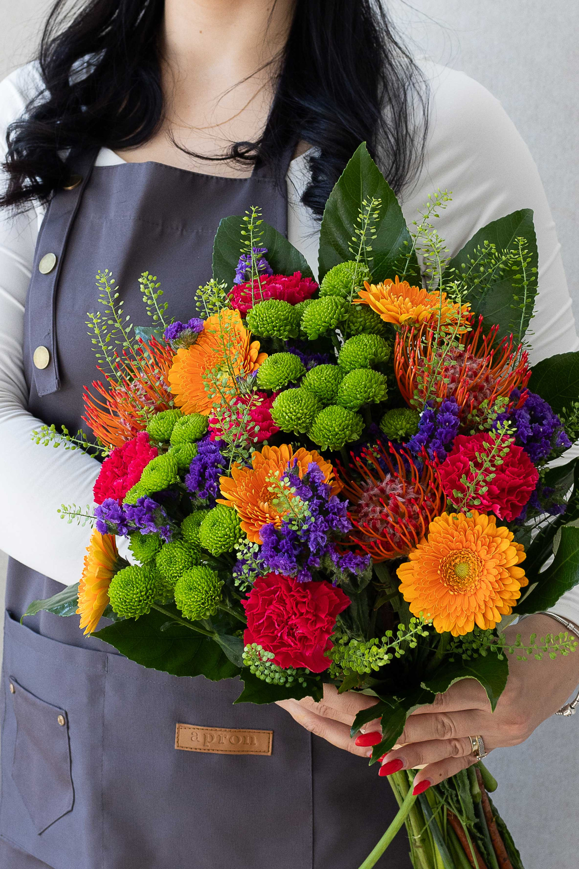 Hand-tied bouquet with orange gerberas, protea, green chrysanthemums, and pink carnations.
