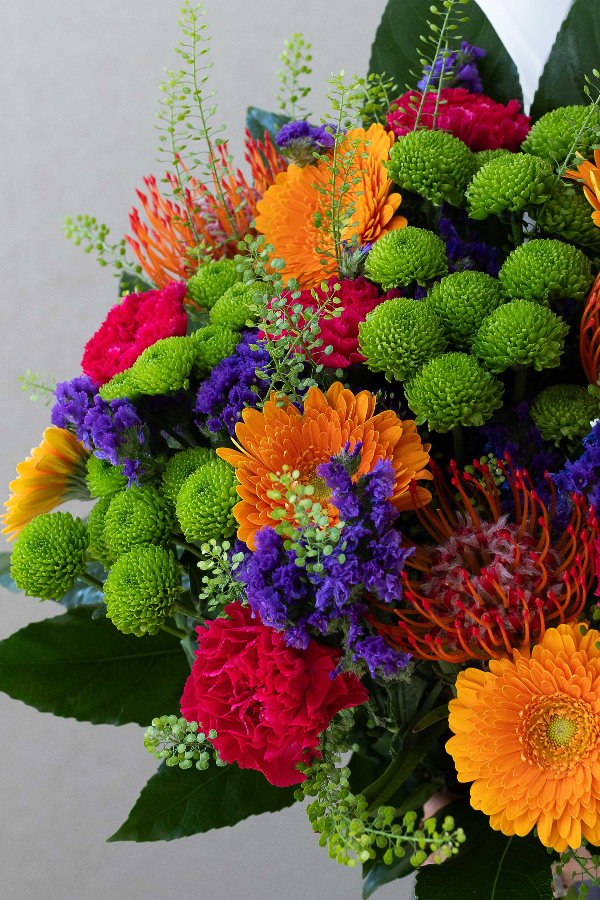 Close-up of orange gerberas, protea, green chrysanthemums, and purple statice.