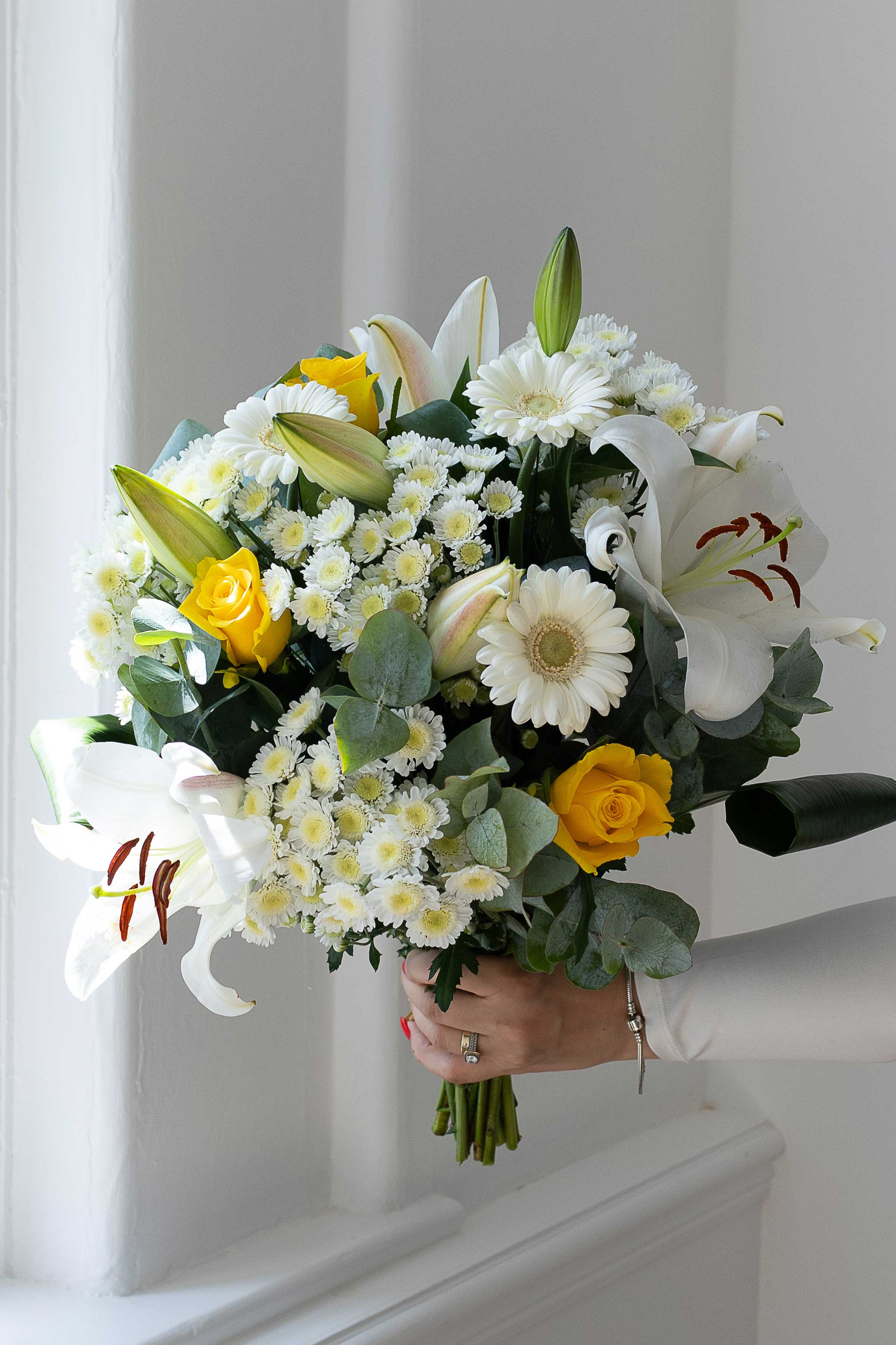 White and yellow bouquet with lilies, roses, and gerberas.