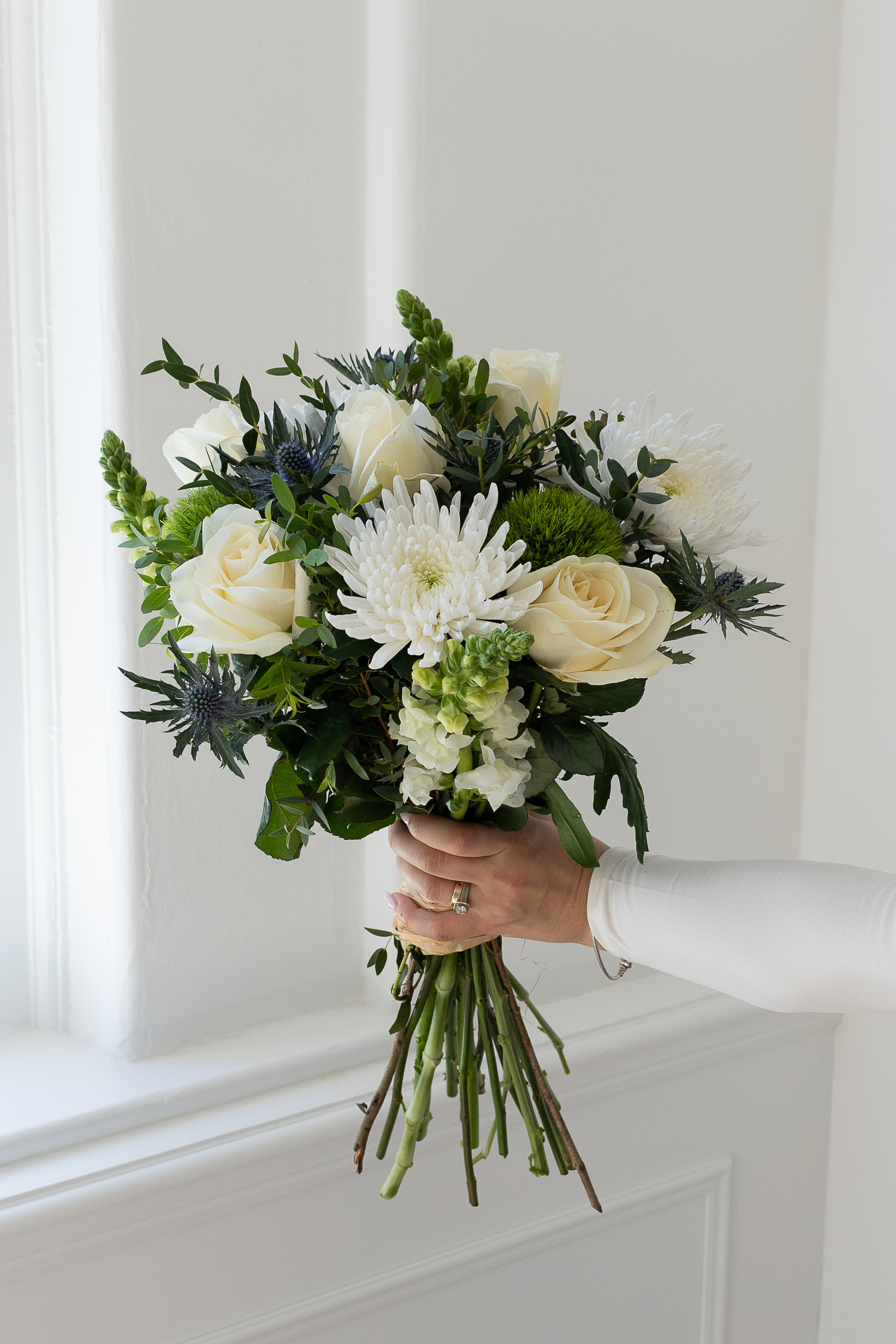 White and green bouquet with roses, chrysanthemums, and thistles.