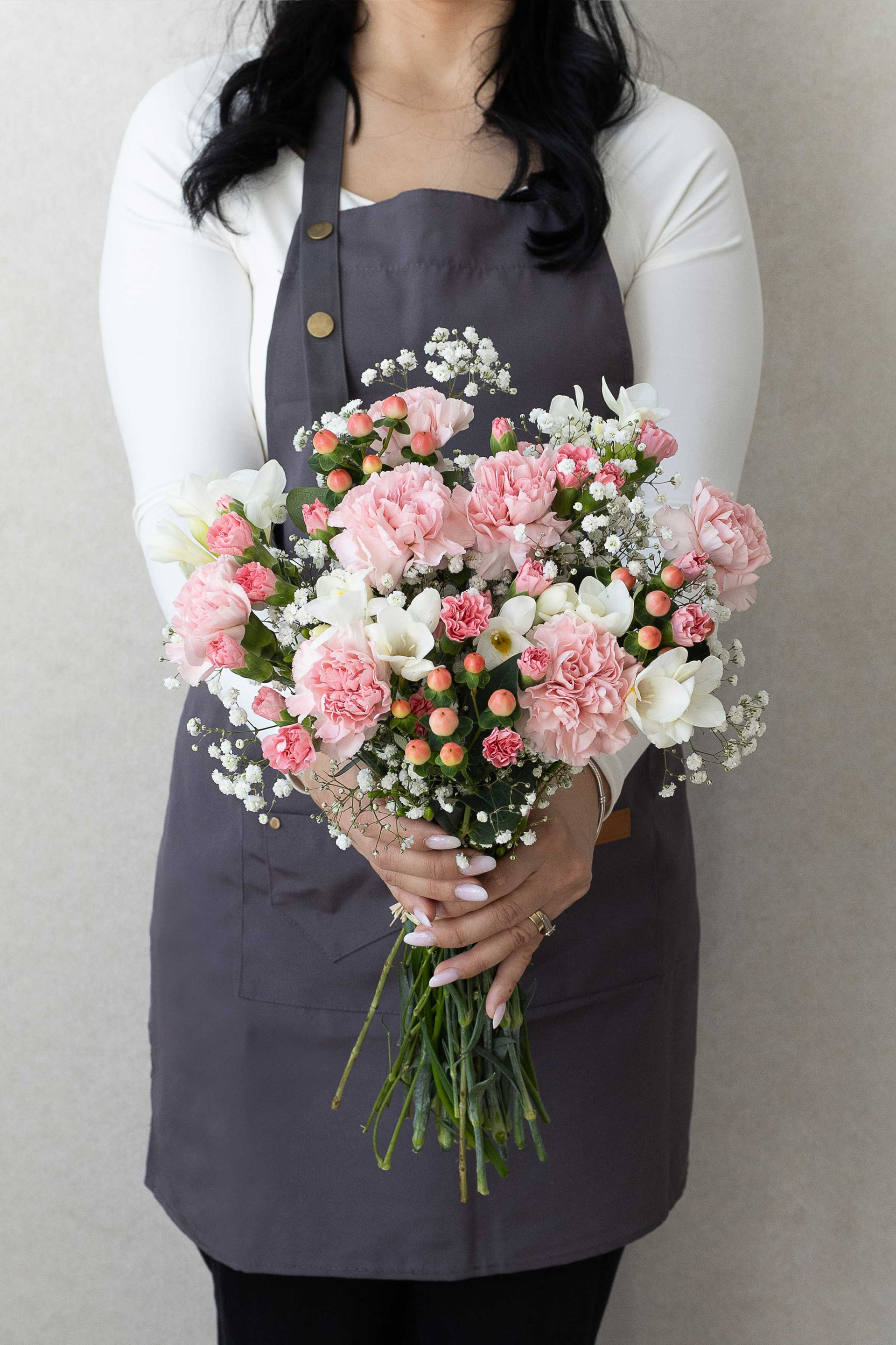 Hand-tied bouquet of pink carnations, white freesia, and gypsophila.