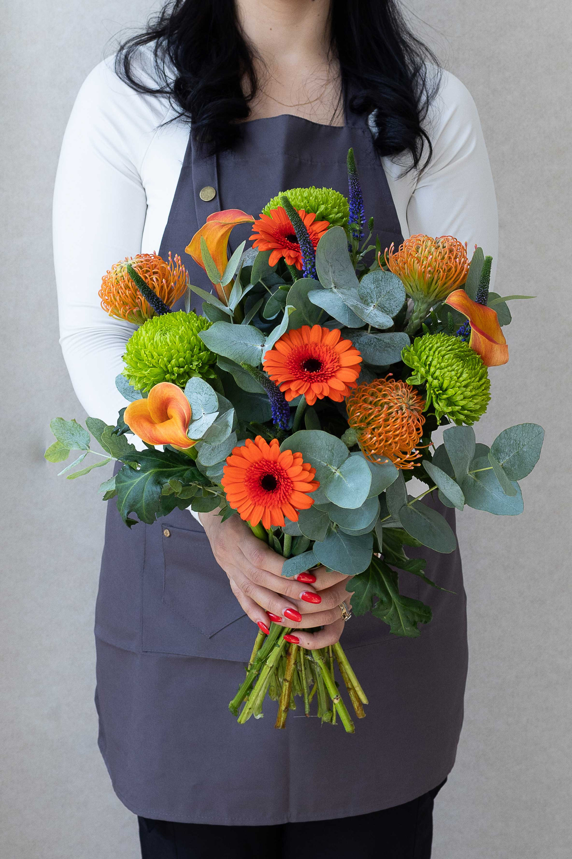 Hand-tied bouquet with orange gerberas, proteas, calla lilies, and greenery.