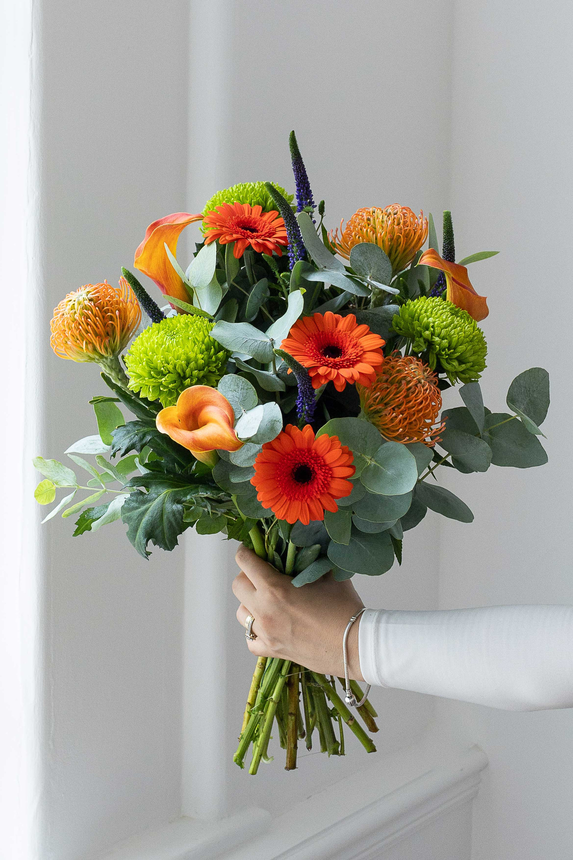 Modern bouquet with orange gerberas, proteas, calla lilies, and eucalyptus.