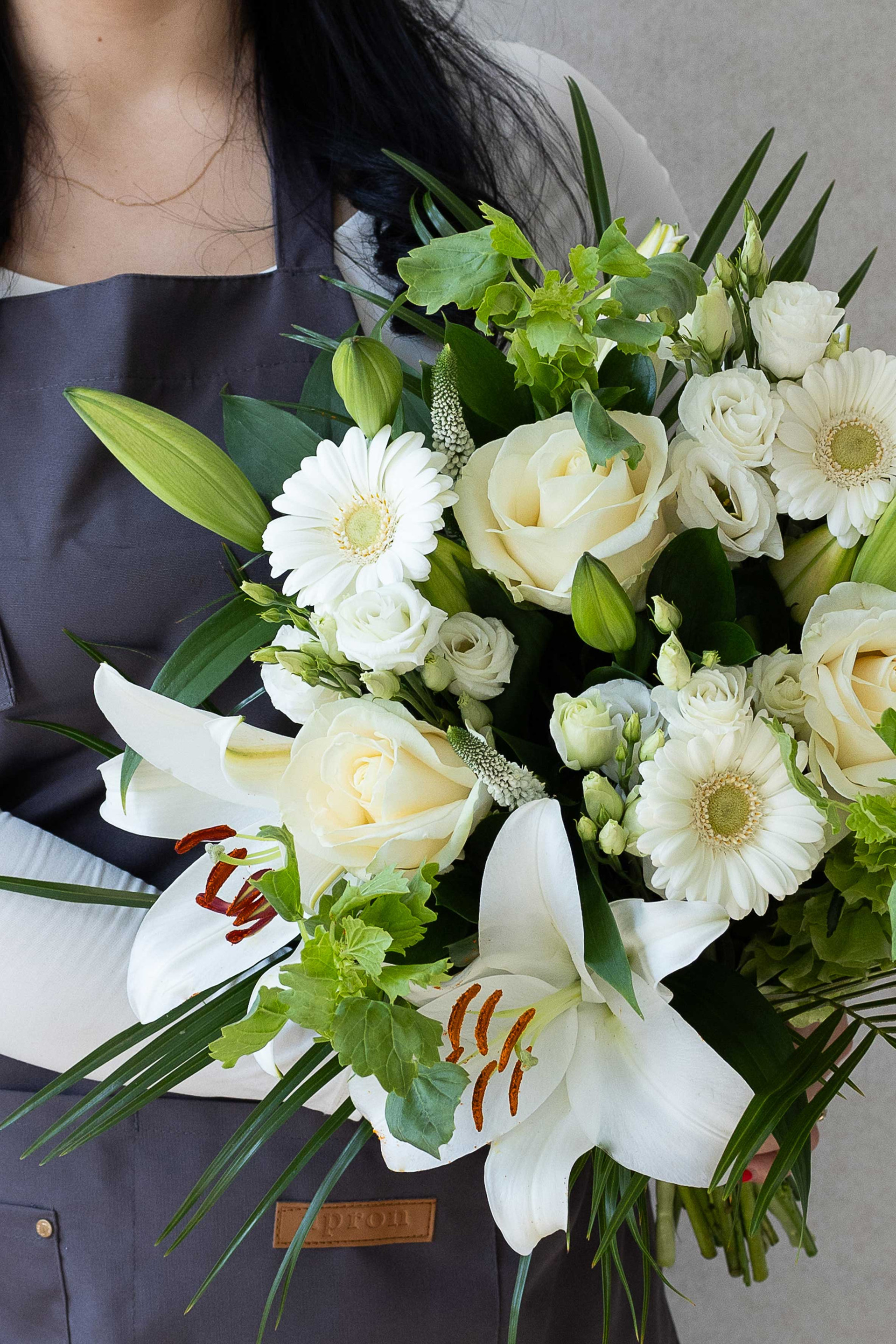 White lily, rose, and germini bouquet with fresh green foliage.