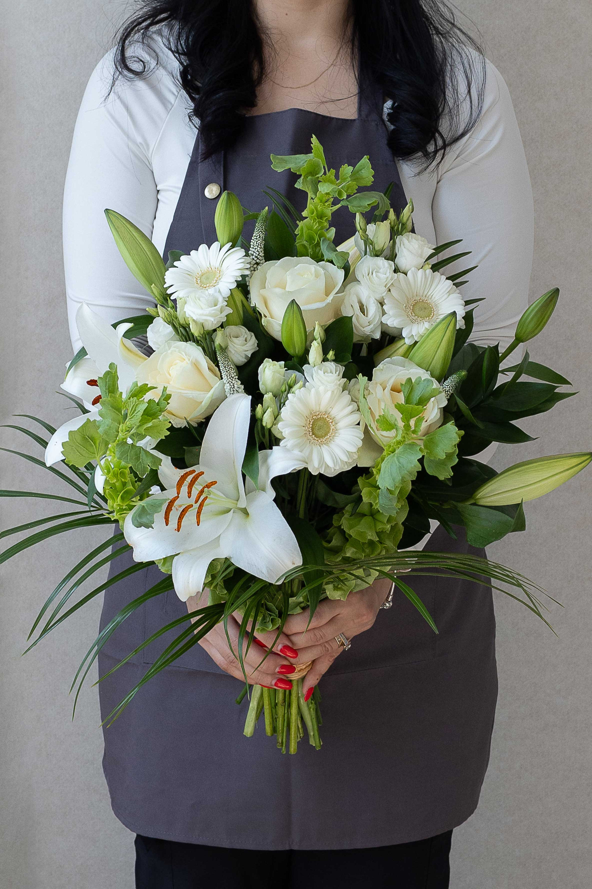 Hand-tied white bouquet with lilies, roses, germini daisies, and greenery.