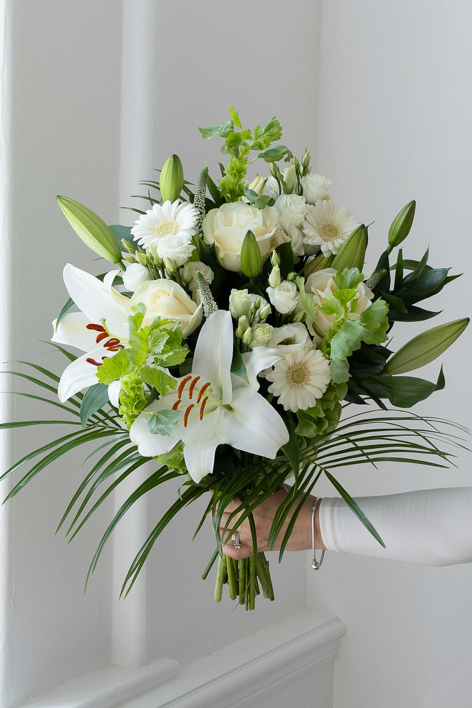 Elegant white bouquet with lilies, roses, germini daisies, and greenery.