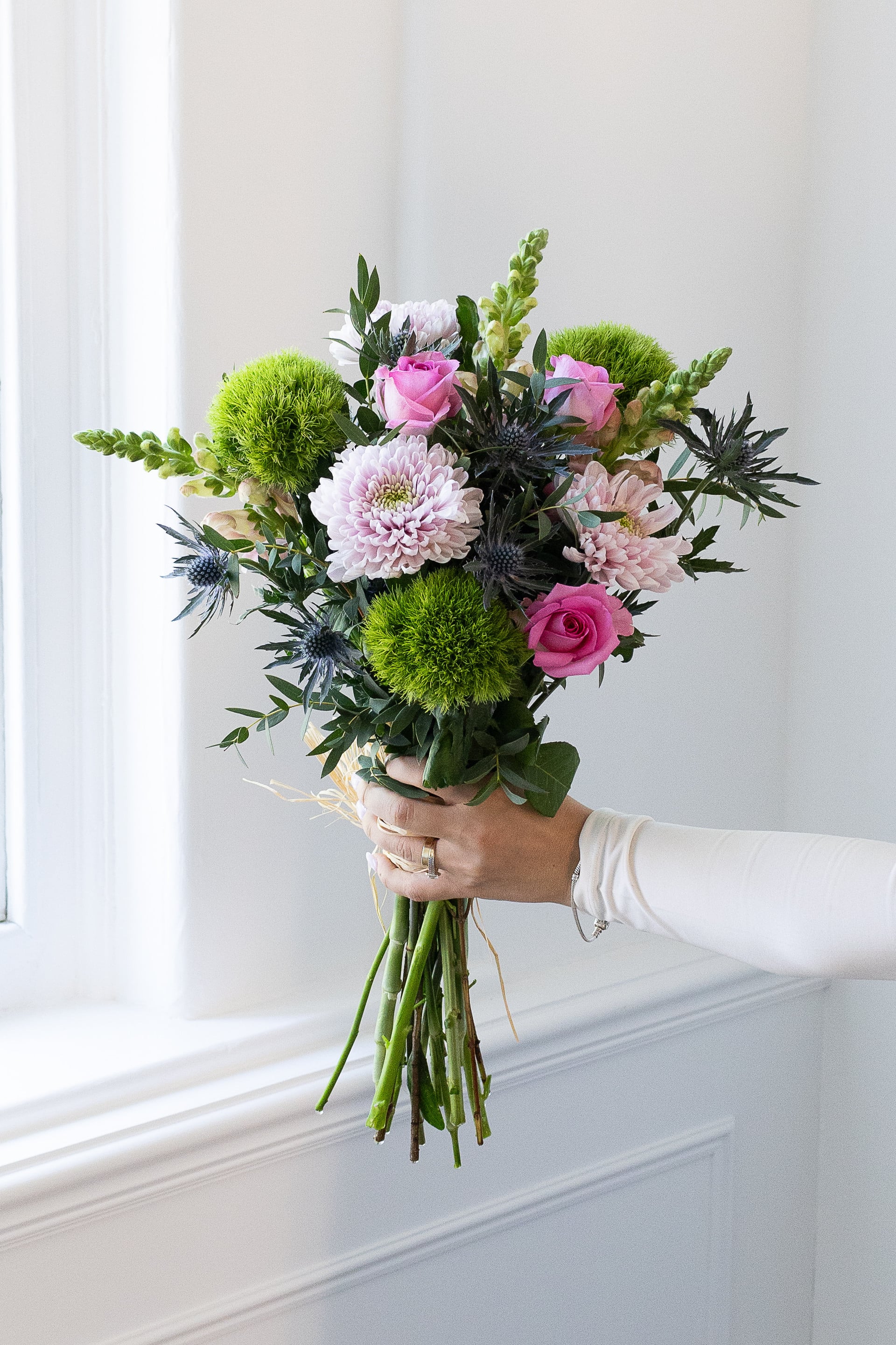 Modern bouquet with pink roses, green dianthus, and thistles.