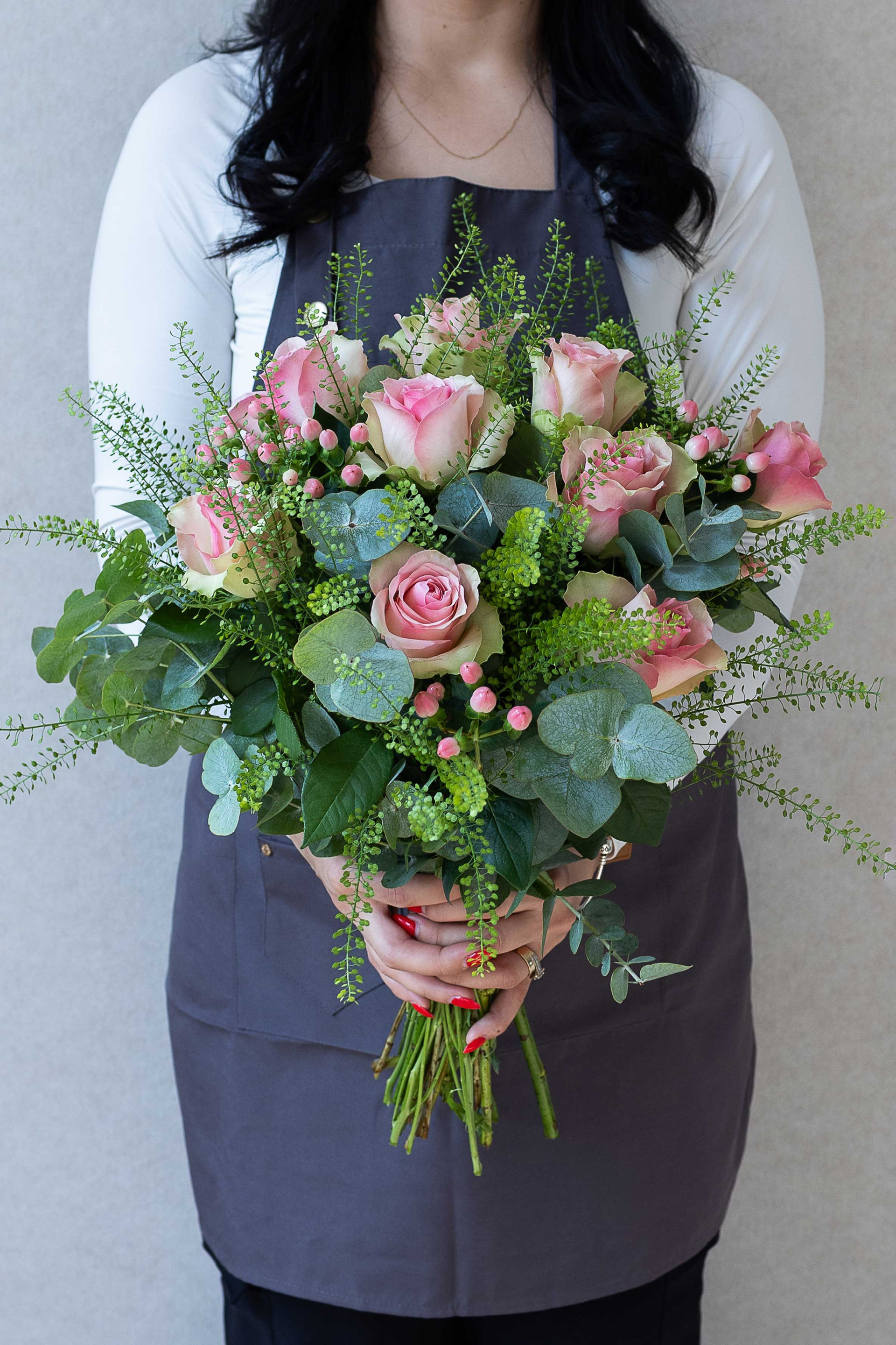 Florist holding a pink rose bouquet with lush greenery.
