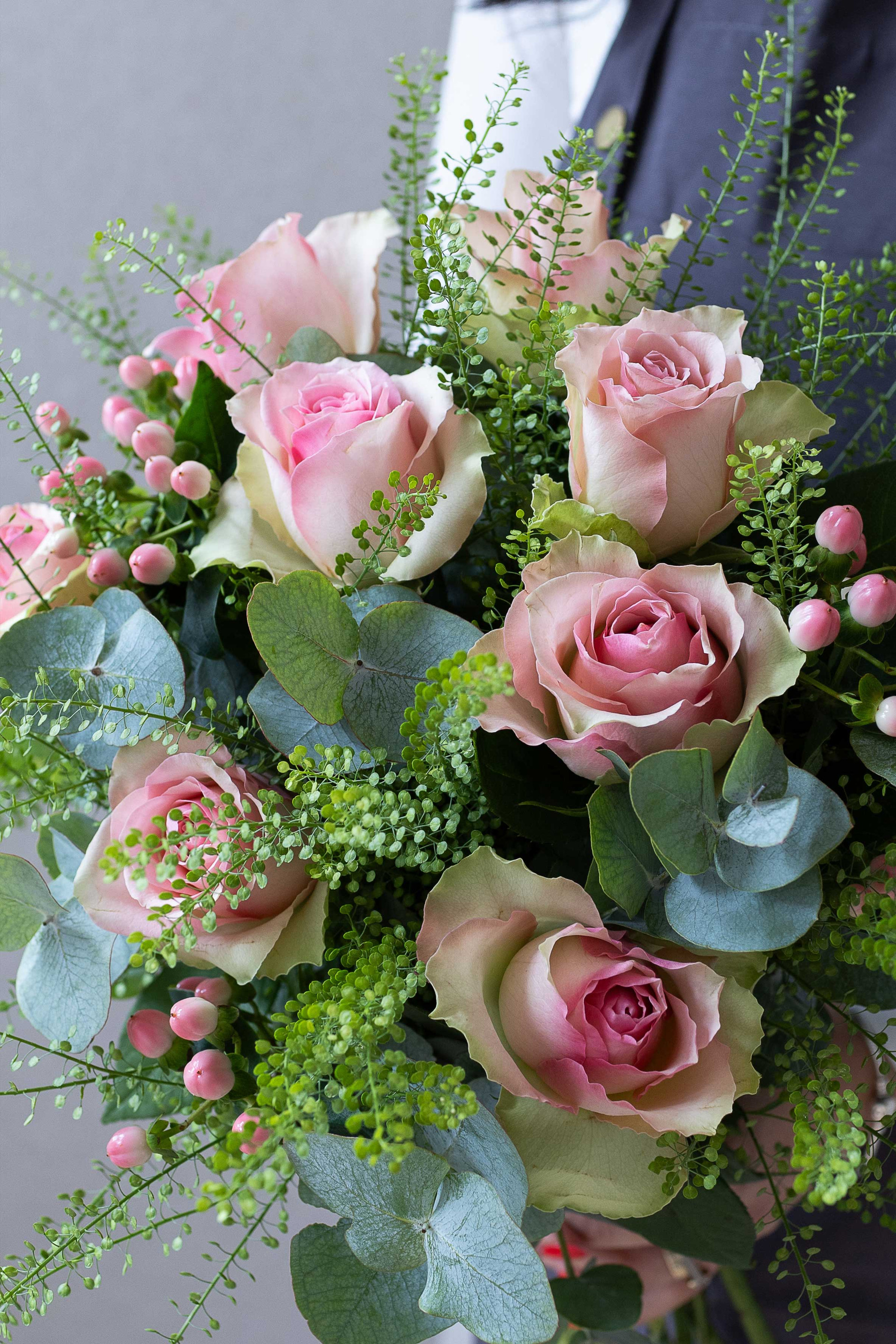 Close-up of pink roses, berries, and eucalyptus foliage.