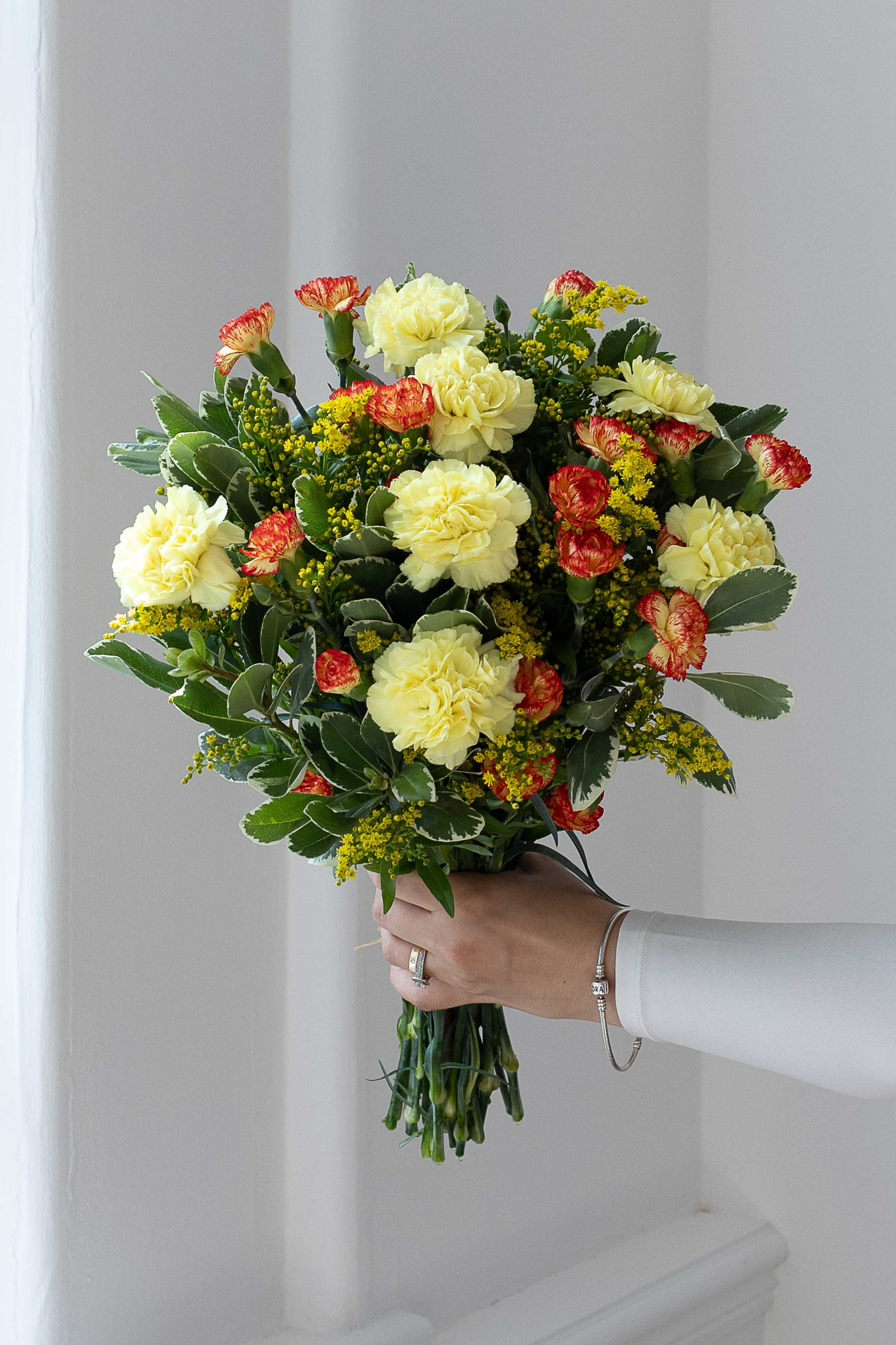 Yellow and orange carnations with yellow solidago and greenery.
