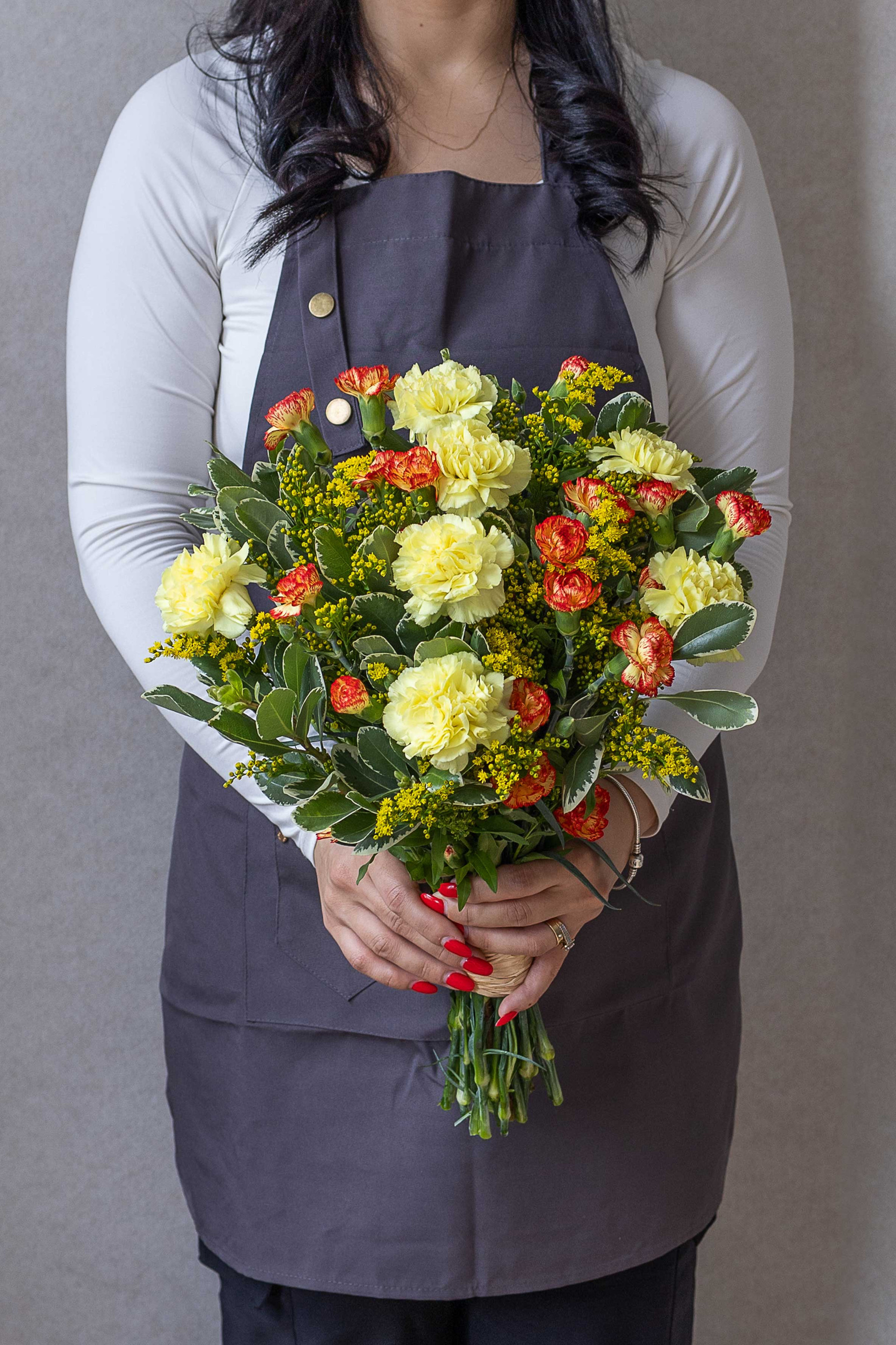 Florist holding a bouquet of yellow and orange carnations with yellow accents.