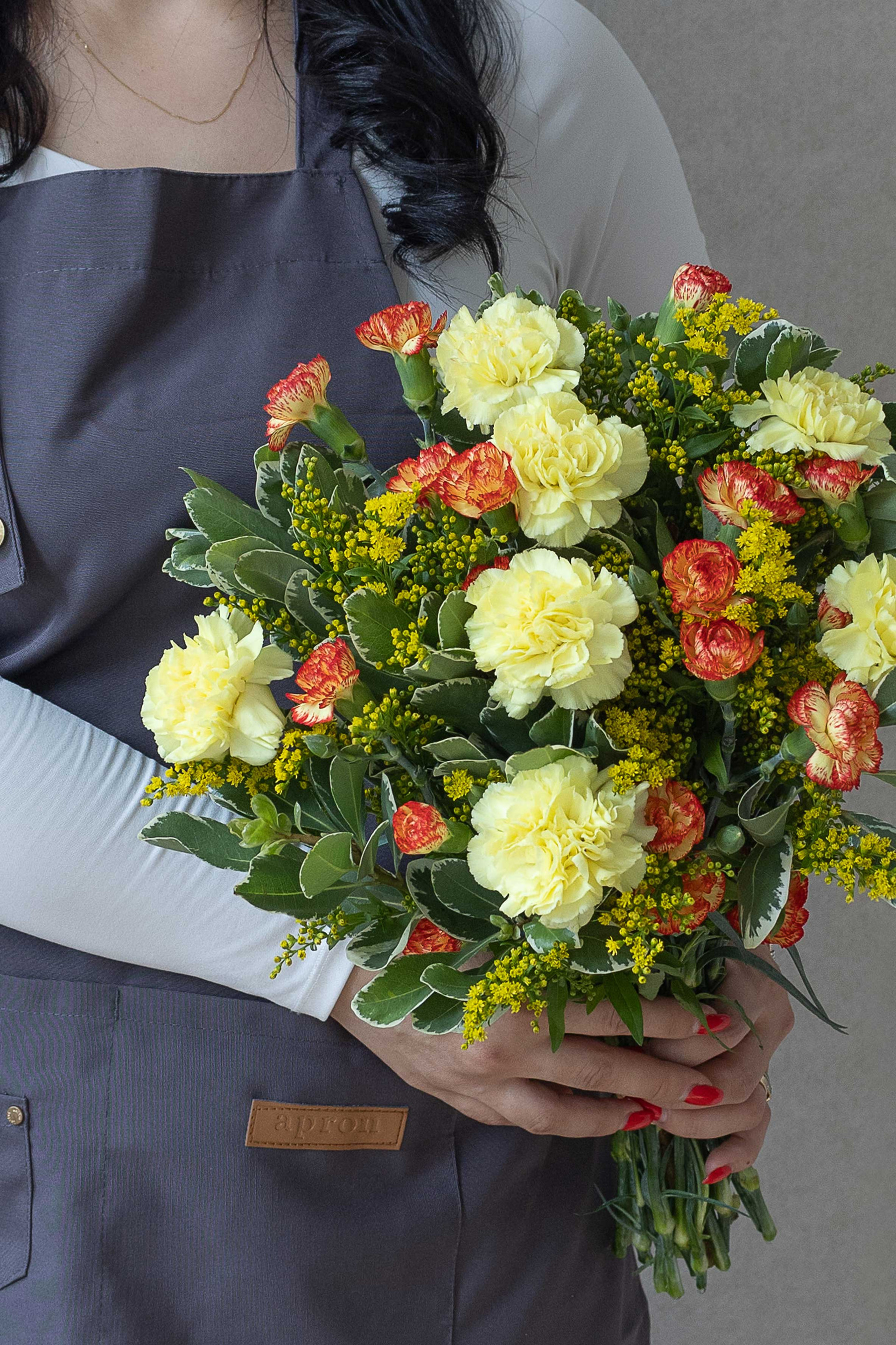 Carnation bouquet with yellow blooms, orange accents, and yellow solidago.