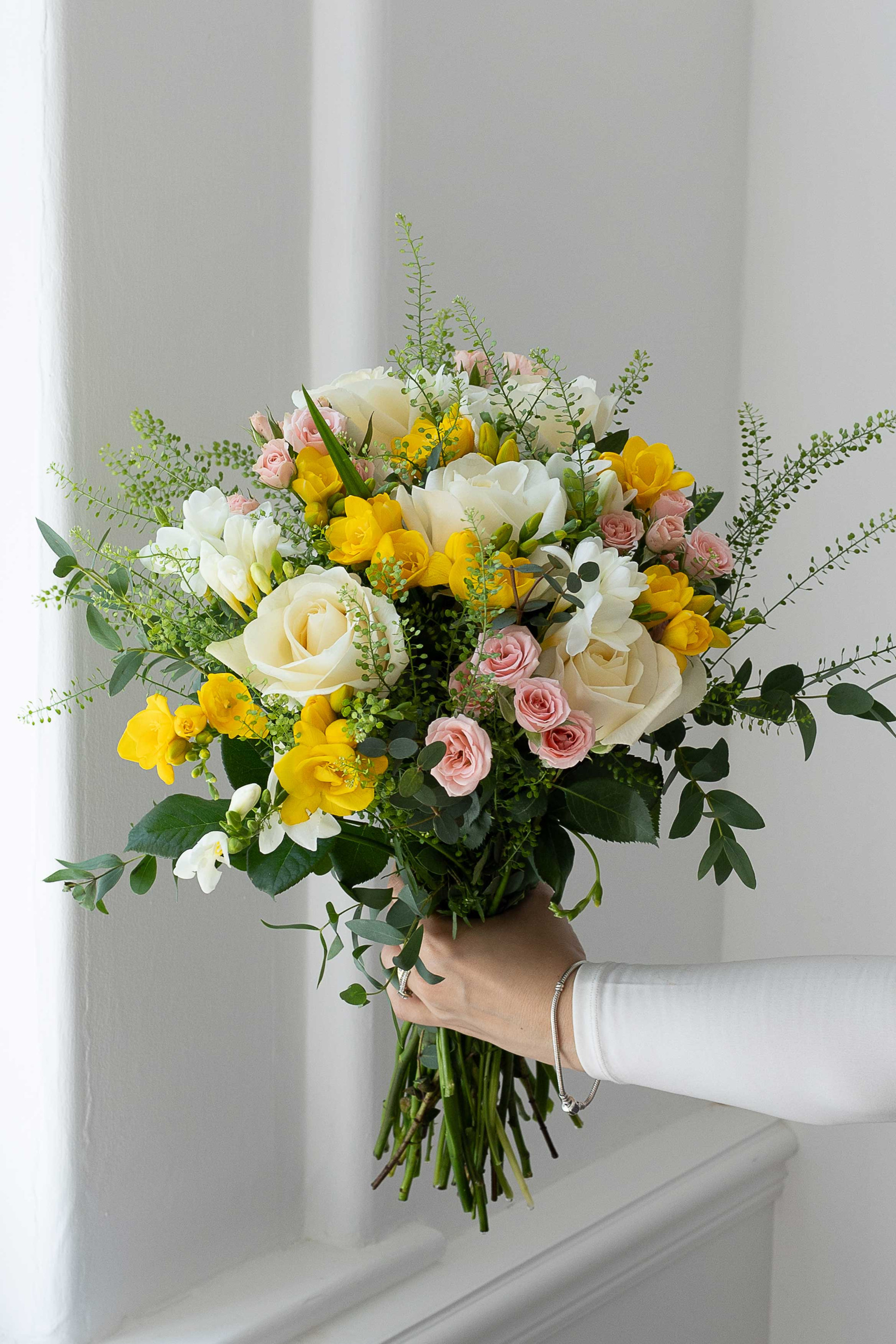Bouquet with white roses, yellow freesia, pink roses, and greenery.