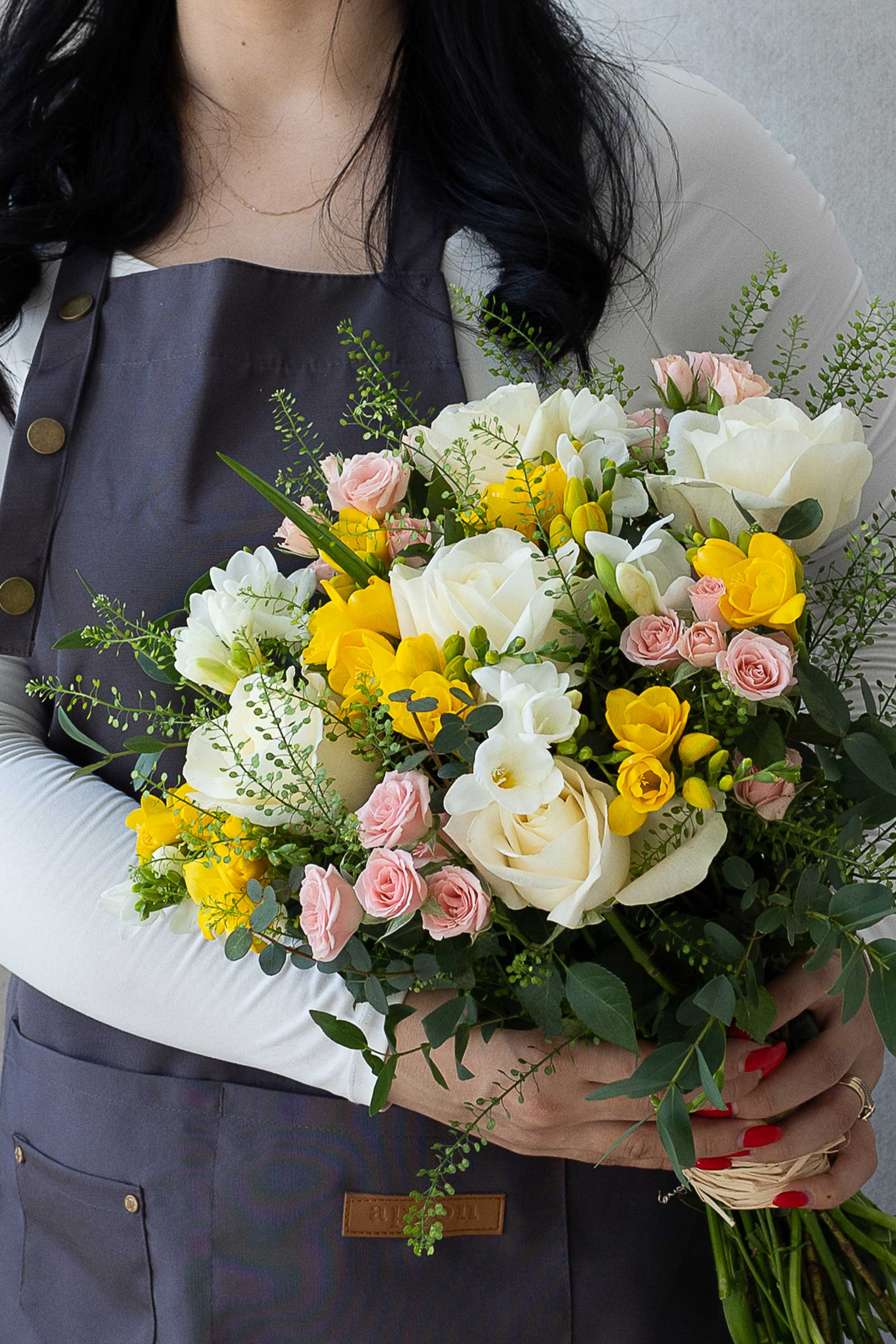Florist holding a white, yellow, and blush pink hand-tied bouquet.