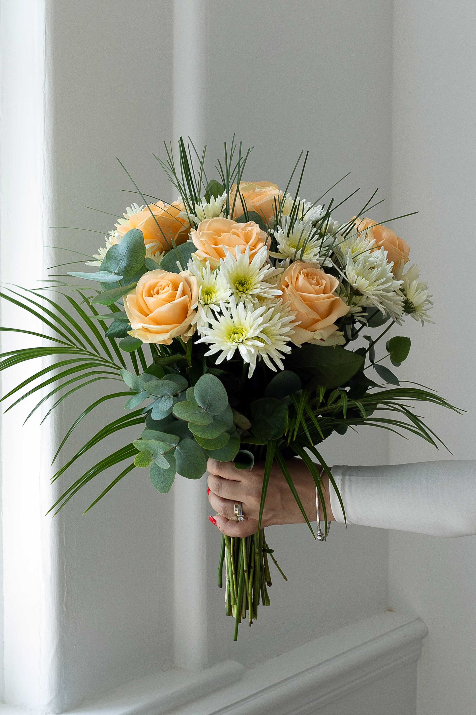 Peach and white bouquet with roses, chrysanthemums, eucalyptus, and palm leaves.