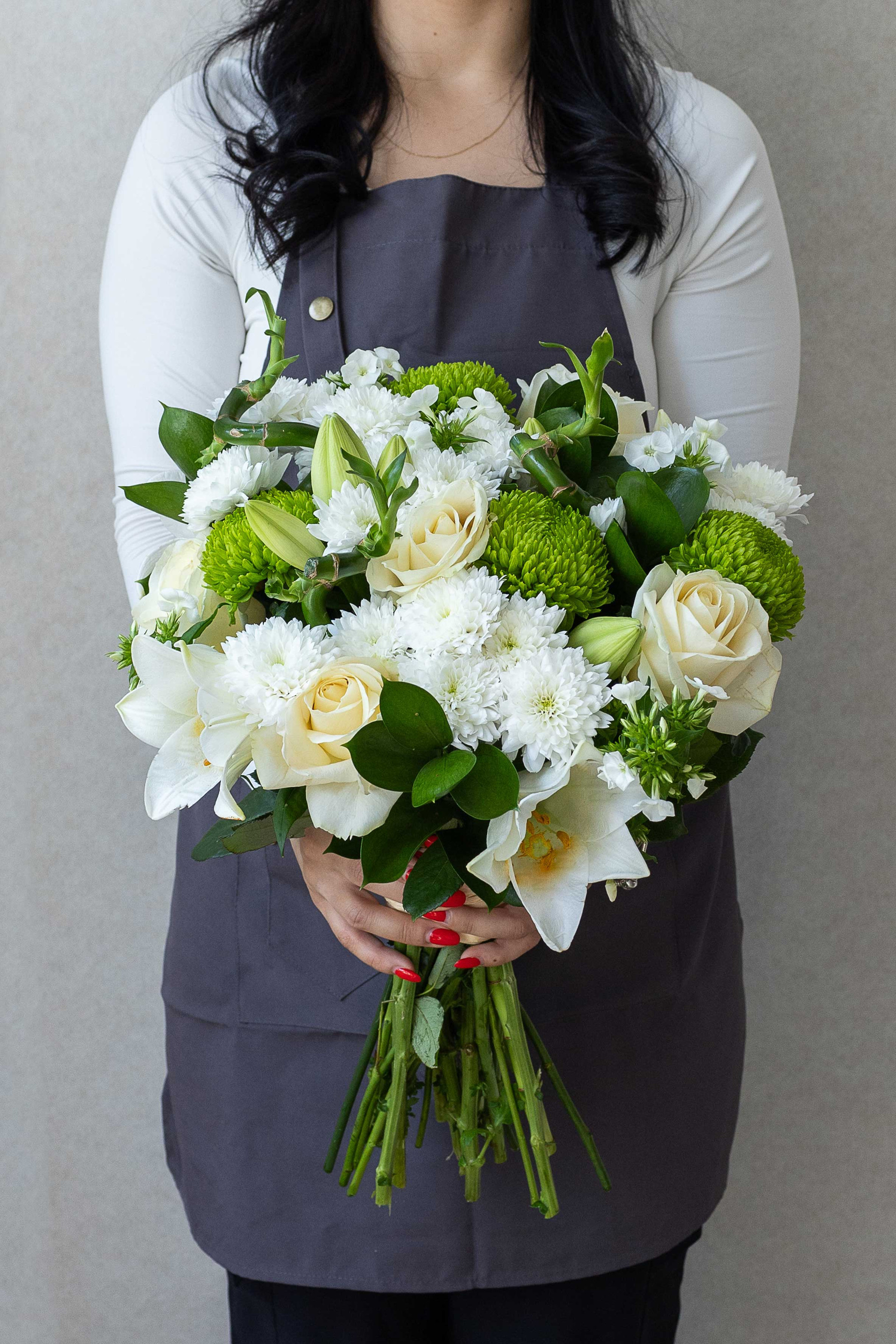Florist holding a white and green bouquet with roses, lilies, and chrysanthemums.