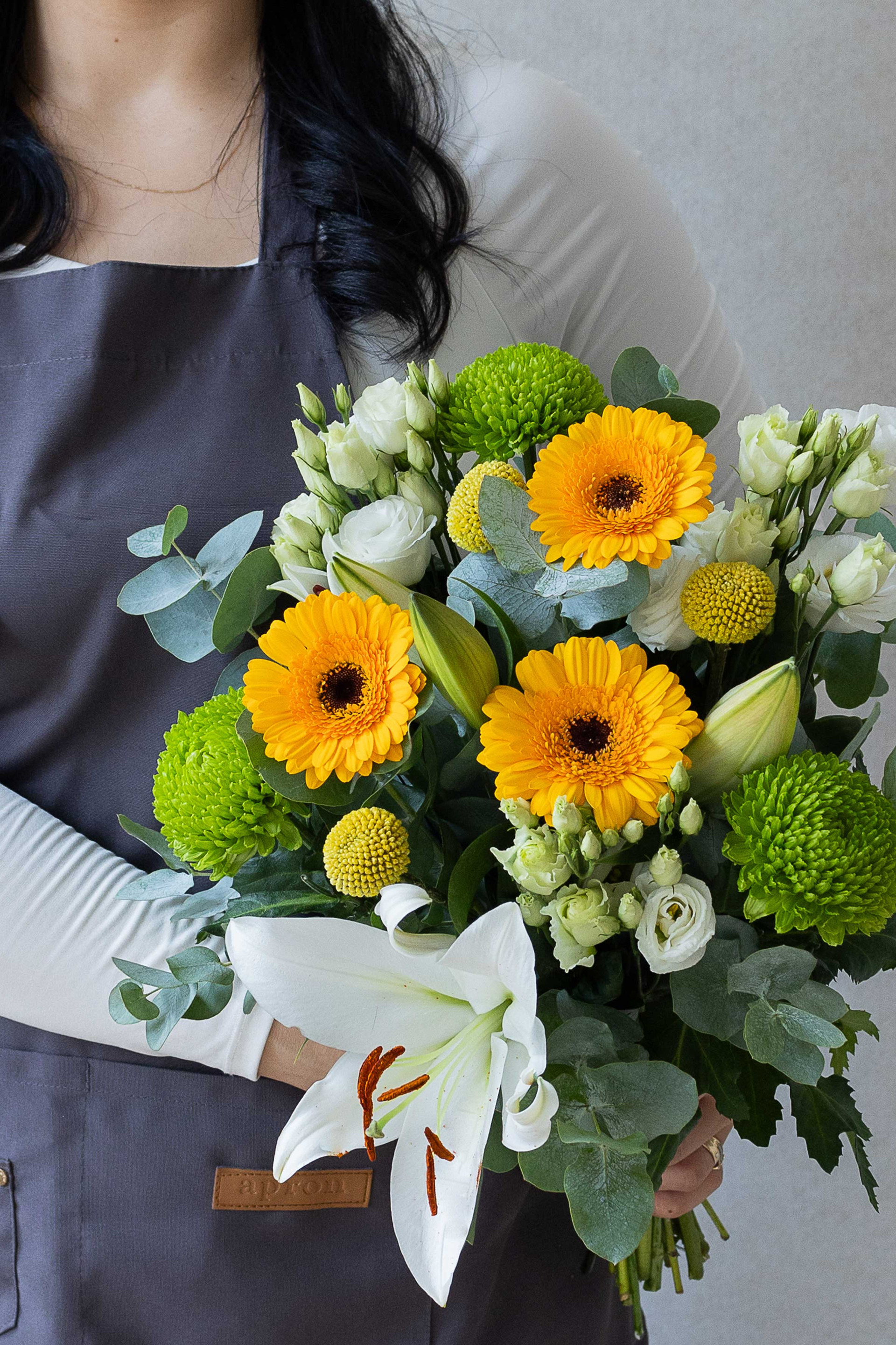 Florist holding a bouquet of yellow gerberas, white lily, green chrysanthemums, and eucalyptus.