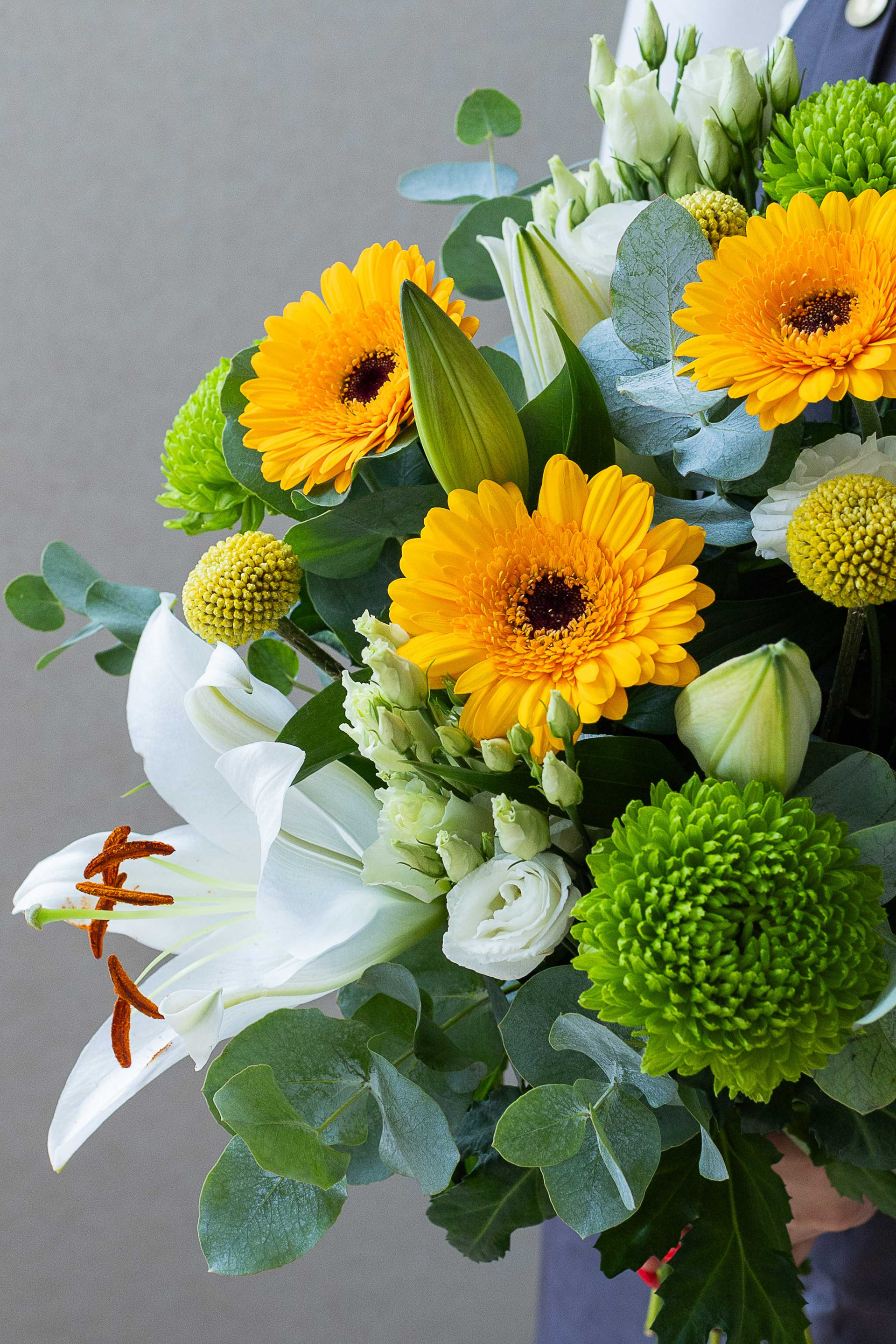 Close-up of yellow gerberas, white lily, green chrysanthemums, and eucalyptus.