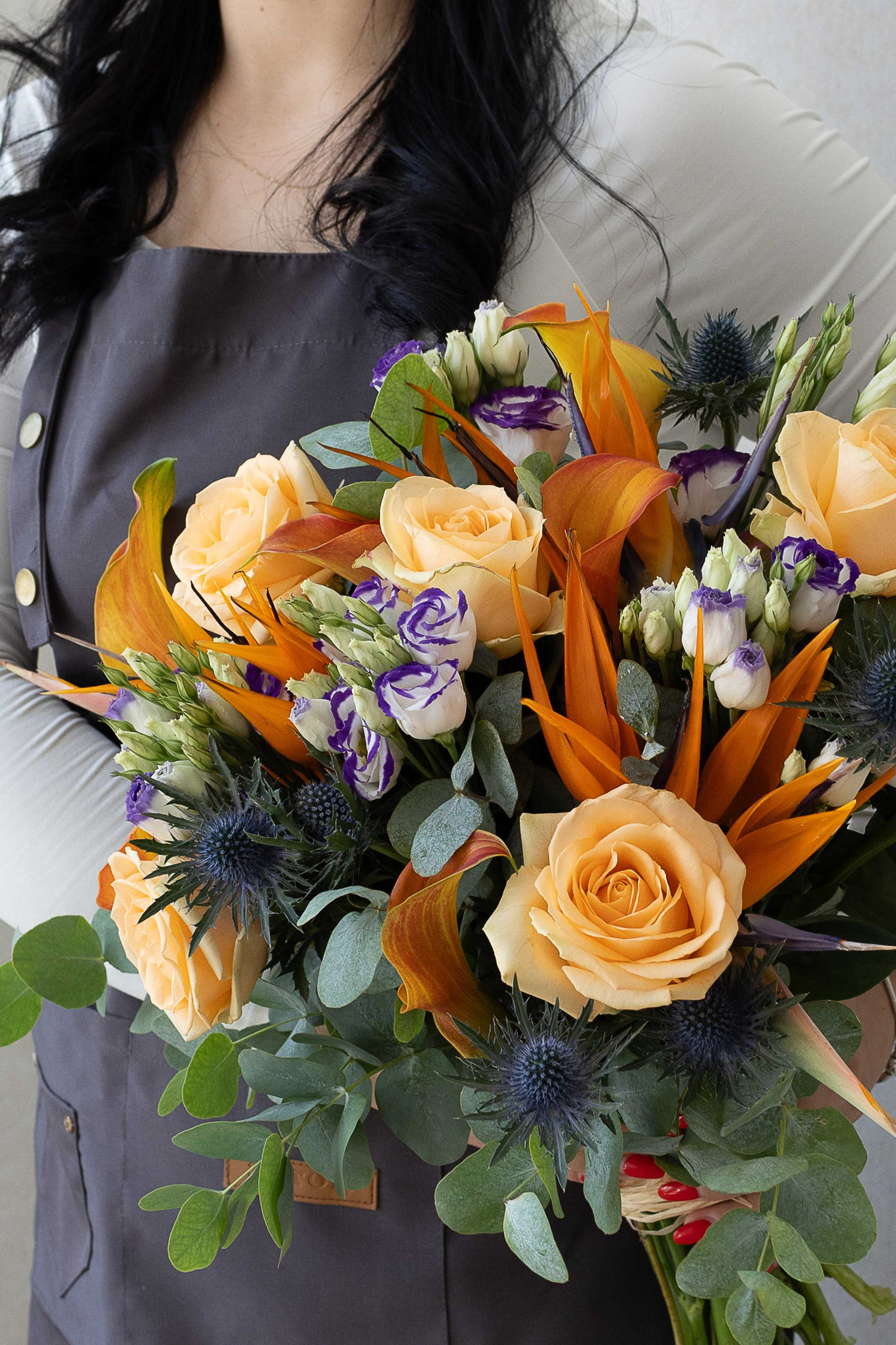 Peach rose and bird of paradise bouquet with lisianthus, thistles, and eucalyptus.