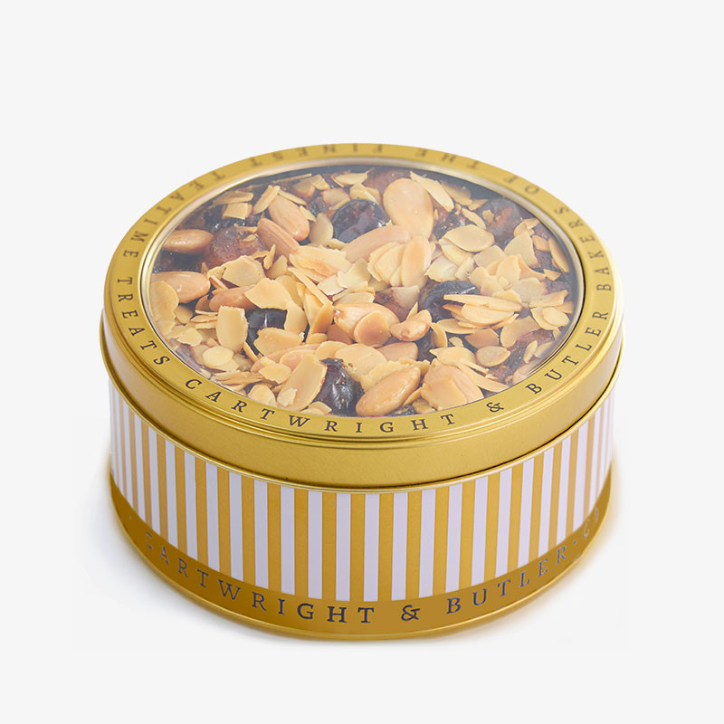 Round gold-striped Cartwright & Butler tin of almond and fruit cake with a clear lid showing toasted almonds and dried fruit.