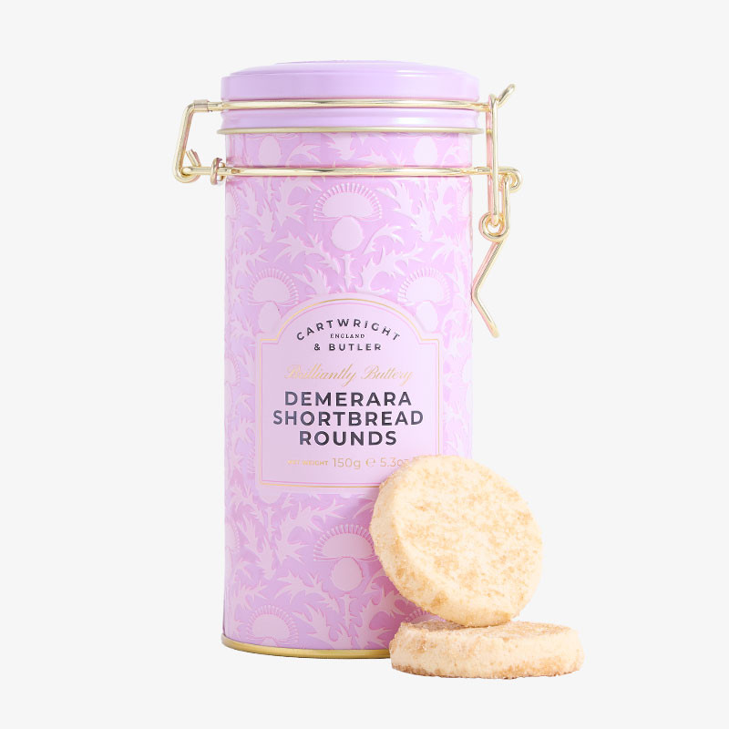 Pastel pink clip-top tin of Cartwright & Butler Demerara Shortbread Rounds with two golden shortbread biscuits displayed in front.