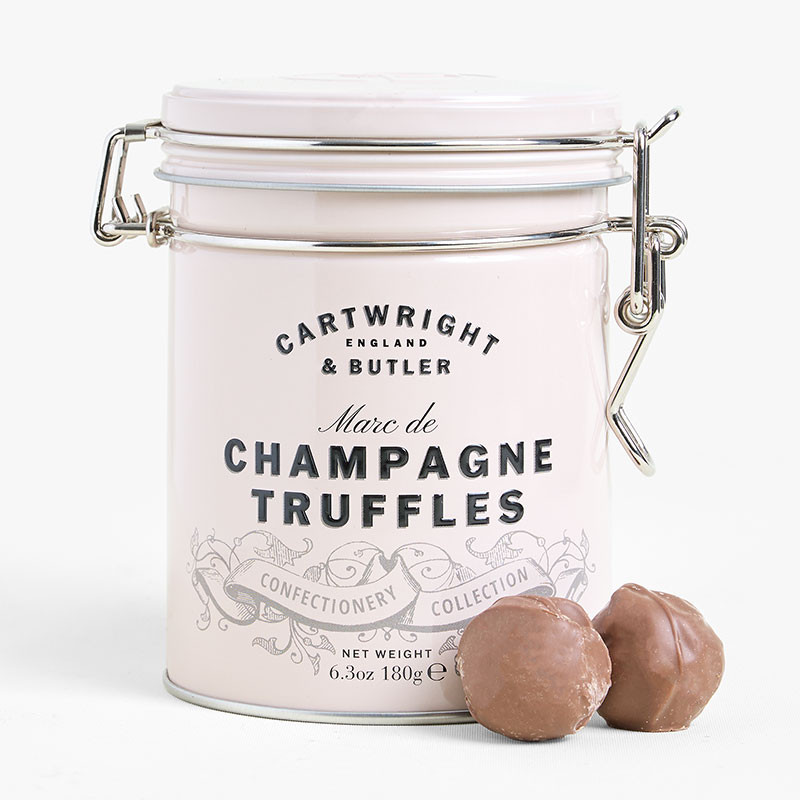 Pale pink clip-top tin of Cartwright & Butler Marc de Champagne Truffles with two milk chocolate truffles displayed in front.