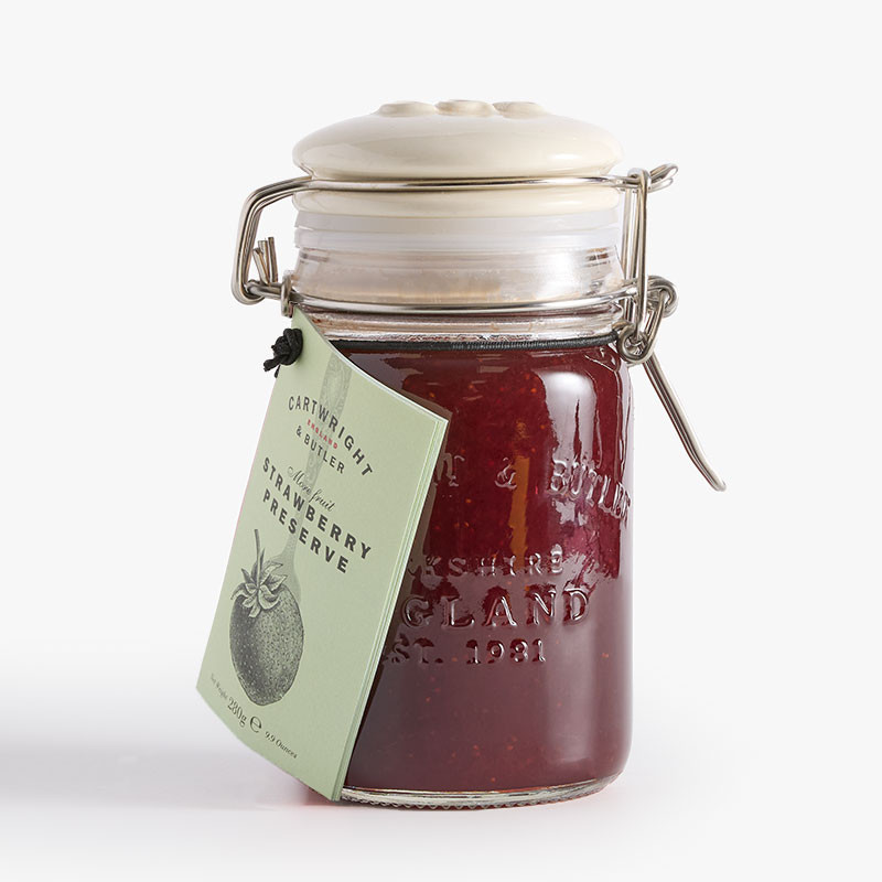 Clip-top glass jar of Cartwright & Butler Strawberry Preserve with a pale green hanging label and rich red preserve visible inside.