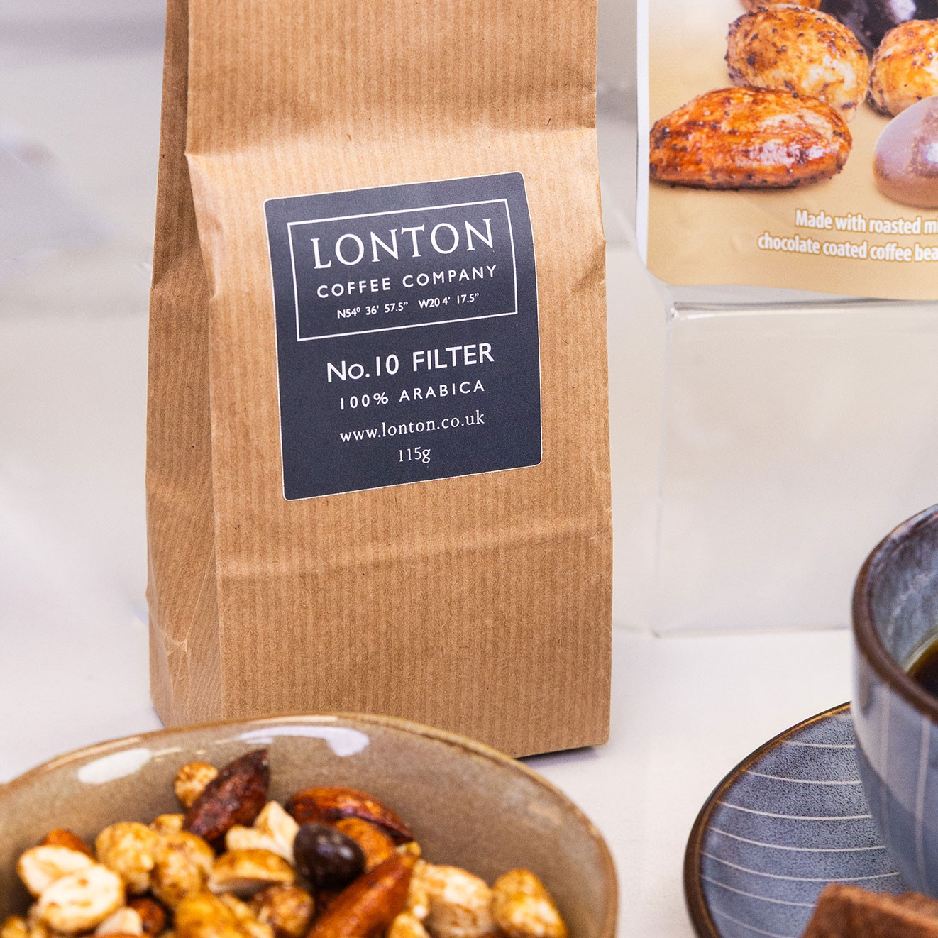 Bag of Lonton Coffee Company No.10 Filter 100% Arabica ground coffee displayed beside coffee and chocolate nut mix.