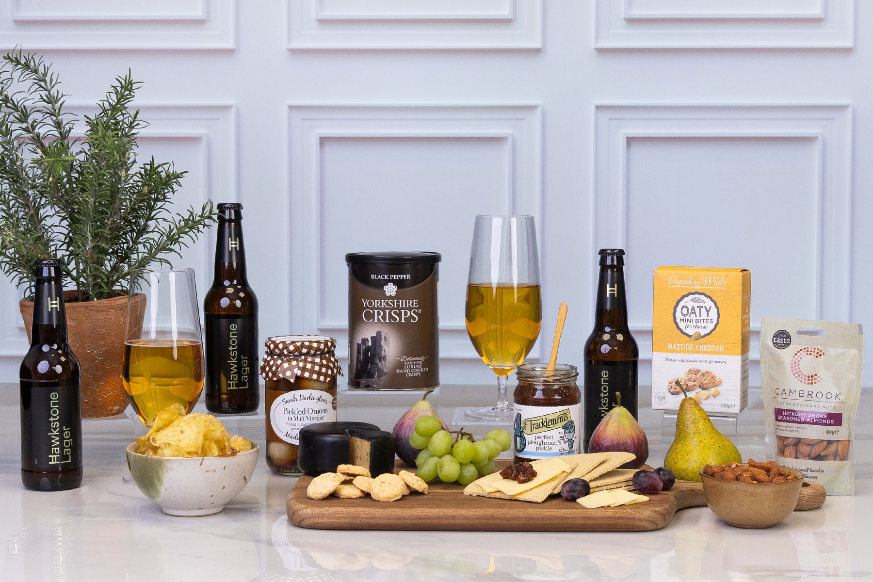 Luxury beer and cheese gift hamper featuring Hawkstone lager, black pepper crisps, mature cheddar mini bites, smoked cheese, crackers, pickled onions, ploughman's pickle, seasoned almonds, fresh fruit and cheese board accompaniments.