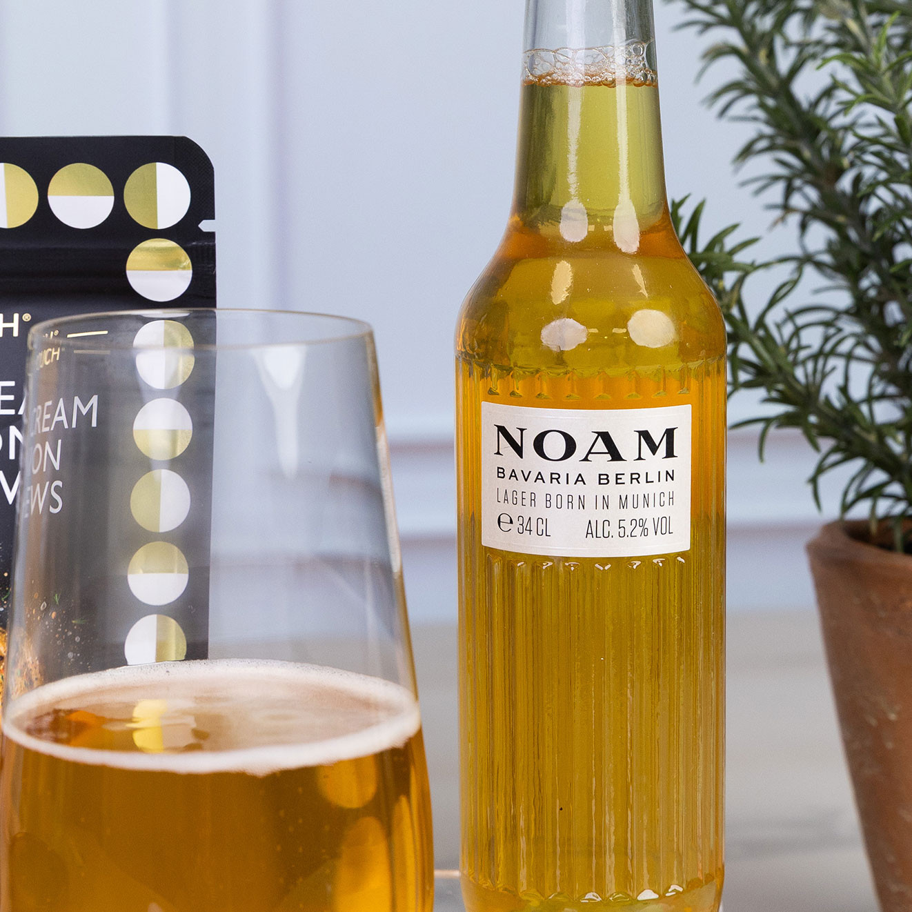 Bottle of NOAM Bavarian Berlin lager served alongside a glass of golden lager.