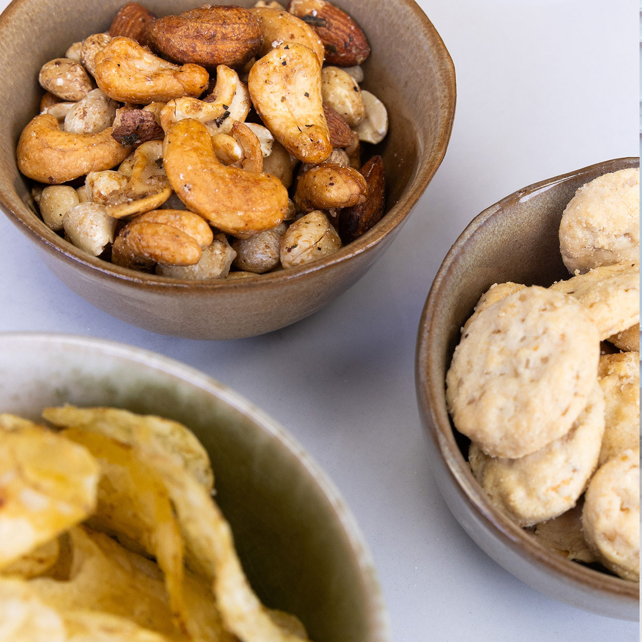 Selection of roasted mixed nuts, oat biscuits and hand cooked crisps served in ceramic bowls.