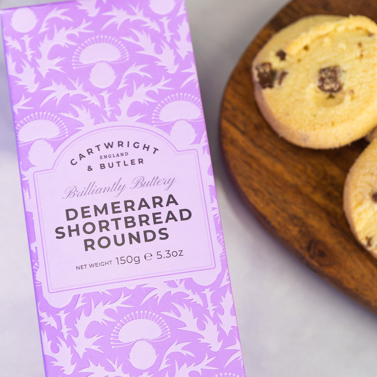 Cartwright & Butler Demerara Shortbread Rounds displayed beside buttery shortbread biscuits on a wooden board.