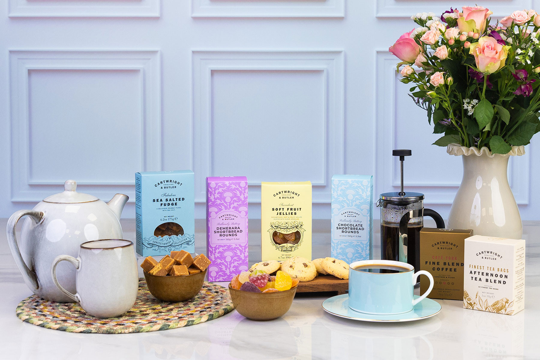 Luxury tea and treats gift set featuring Cartwright & Butler biscuits, sea salted fudge, fruit jellies, coffee, afternoon tea, cafetière and fresh flowers.