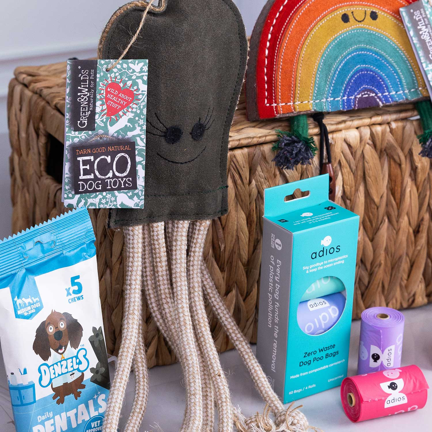 Close up of Selection of eco-friendly dog products including natural treats, dental chews, compostable dog poo bags, and sustainable dog toys displayed in front of a woven storage basket.