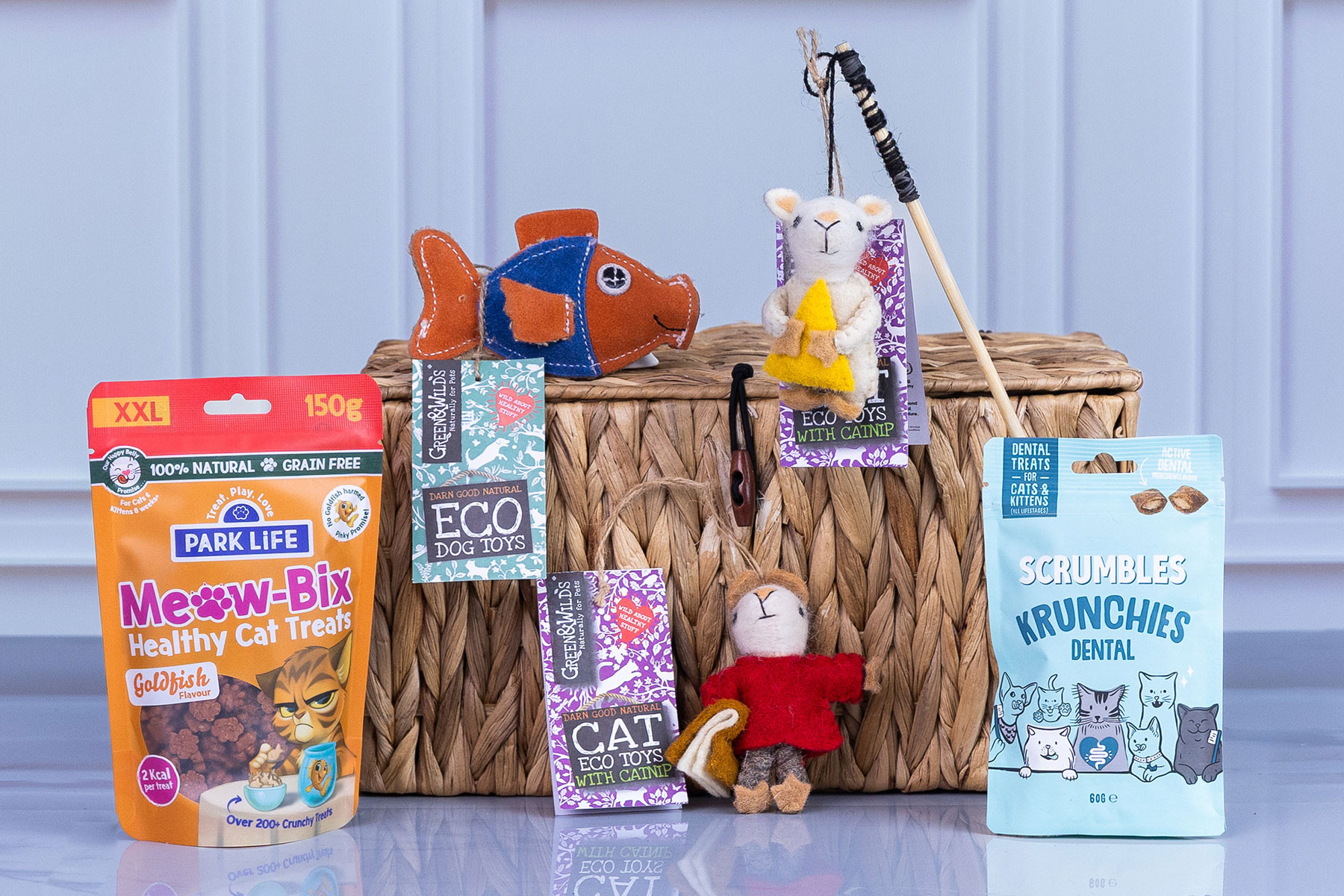 Selection of natural cat treats, dental treats, eco cat toys, and catnip toys displayed in front of a woven storage basket.