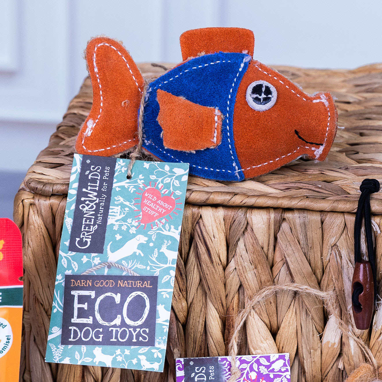 Green & Wild's fish-shaped eco cat toy made with natural materials displayed on a woven basket with product tag attached.