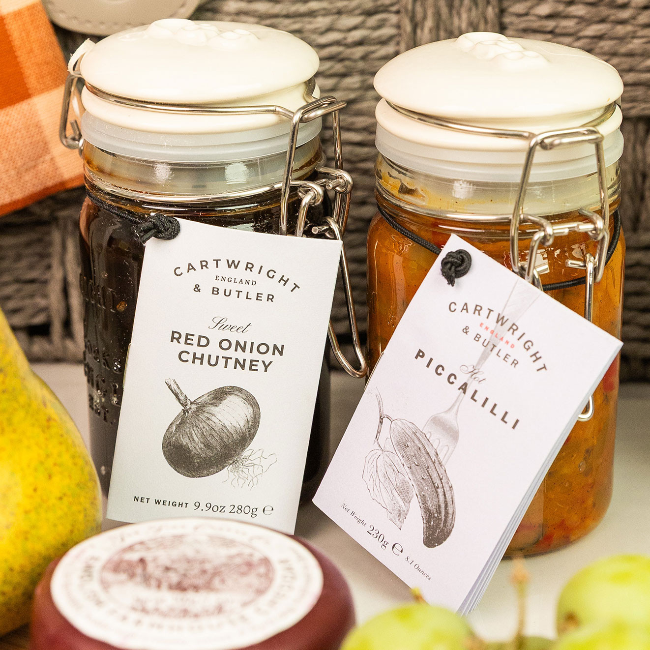 Cartwright & Butler Red Onion Chutney and Hot Piccalilli in clip-top glass jars displayed beside a cheeseboard.