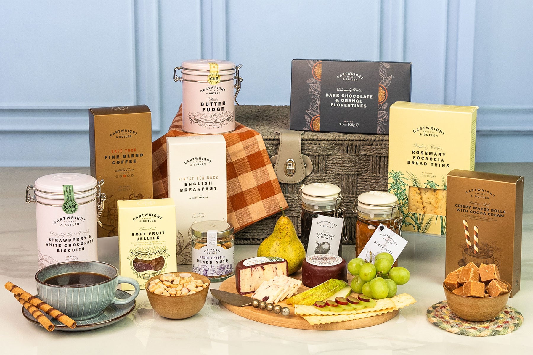 Cartwright & Butler gourmet food hamper featuring coffee, tea, biscuits, fudge, preserves, crackers, cheese, chutney and sweet treats arranged beside a rope hamper.