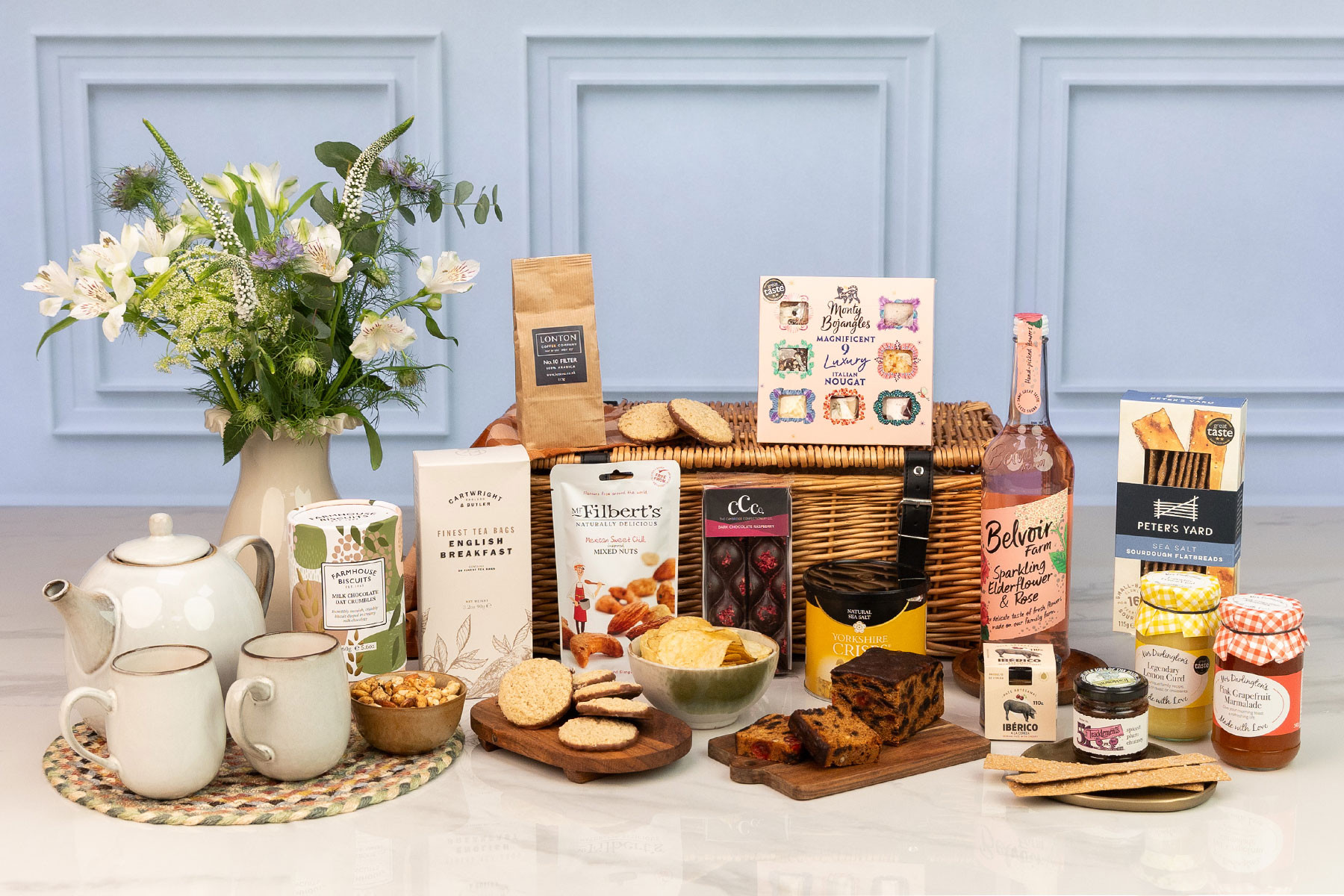 Luxury gourmet hamper with artisan sweet and savoury treats, tea, coffee, sparkling elderflower drink, flowers and a traditional willow basket.